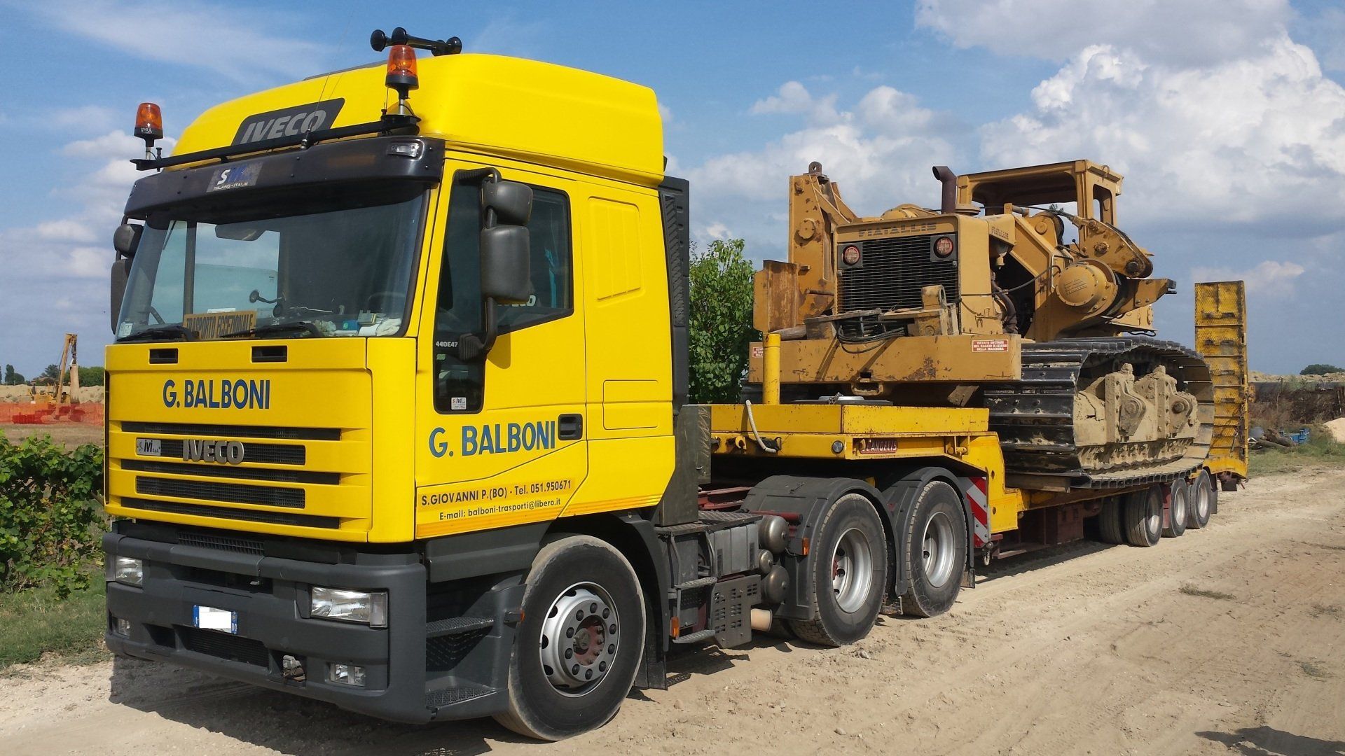 Camion giallo che trasporta un bulldozer su un rimorchio; ambientazione esterna.