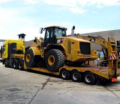 Un caricatore Caterpillar giallo su un rimorchio a pianale trainato da un camion giallo. All'aperto, giornata nuvolosa.