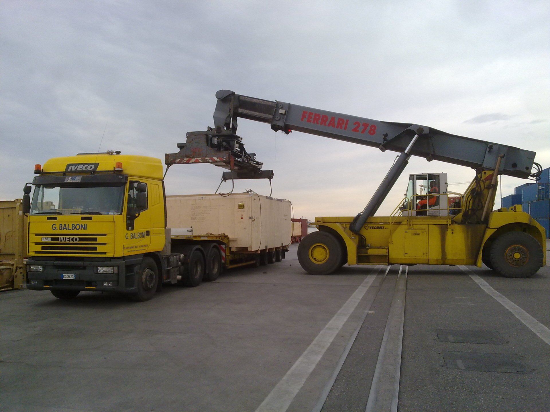 Carrello elevatore giallo che carica un container su un camion giallo in un ambiente industriale.