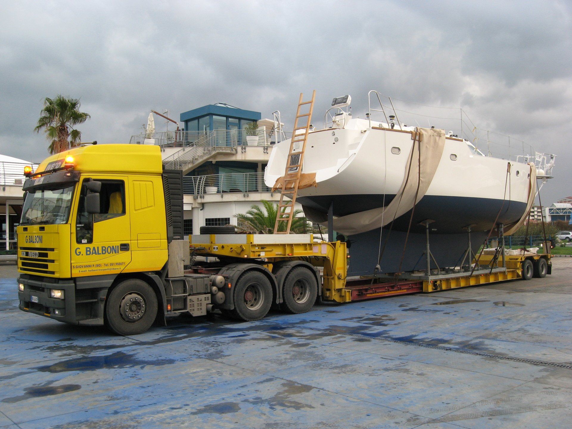 Trattore giallo su un rimorchio a pianale, trainato da un camion giallo, su una strada asfaltata.