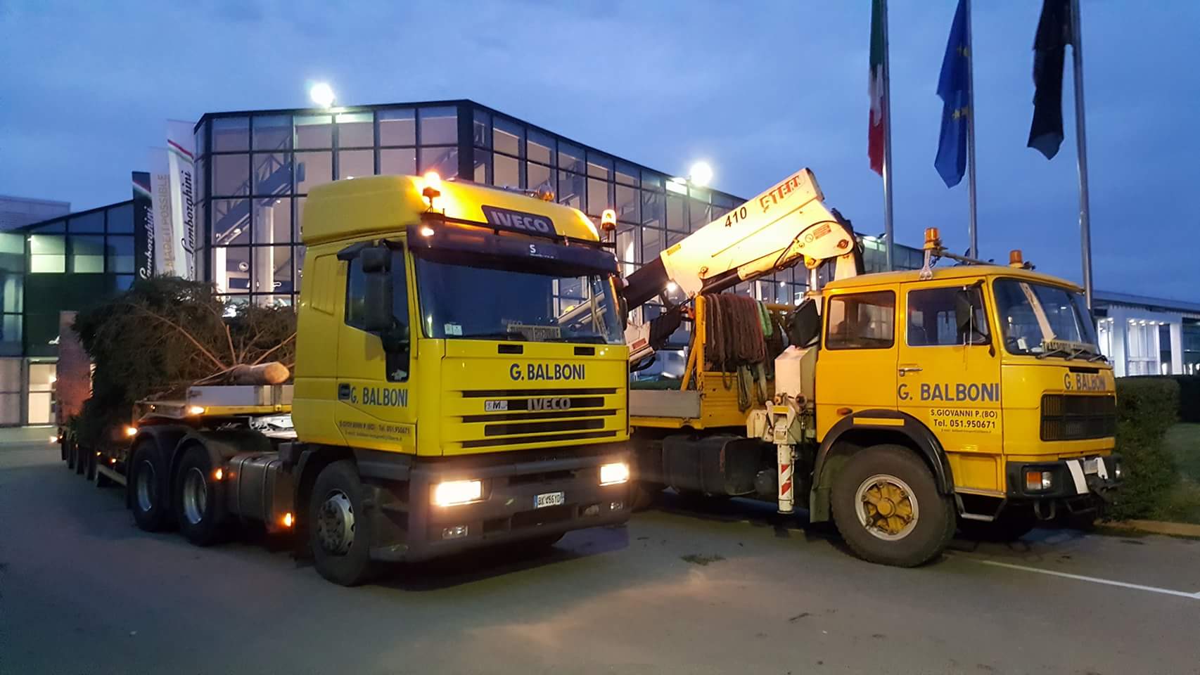 Carrello elevatore giallo su un camion con pianale giallo, parcheggiato su una strada con uno sfondo montuoso.