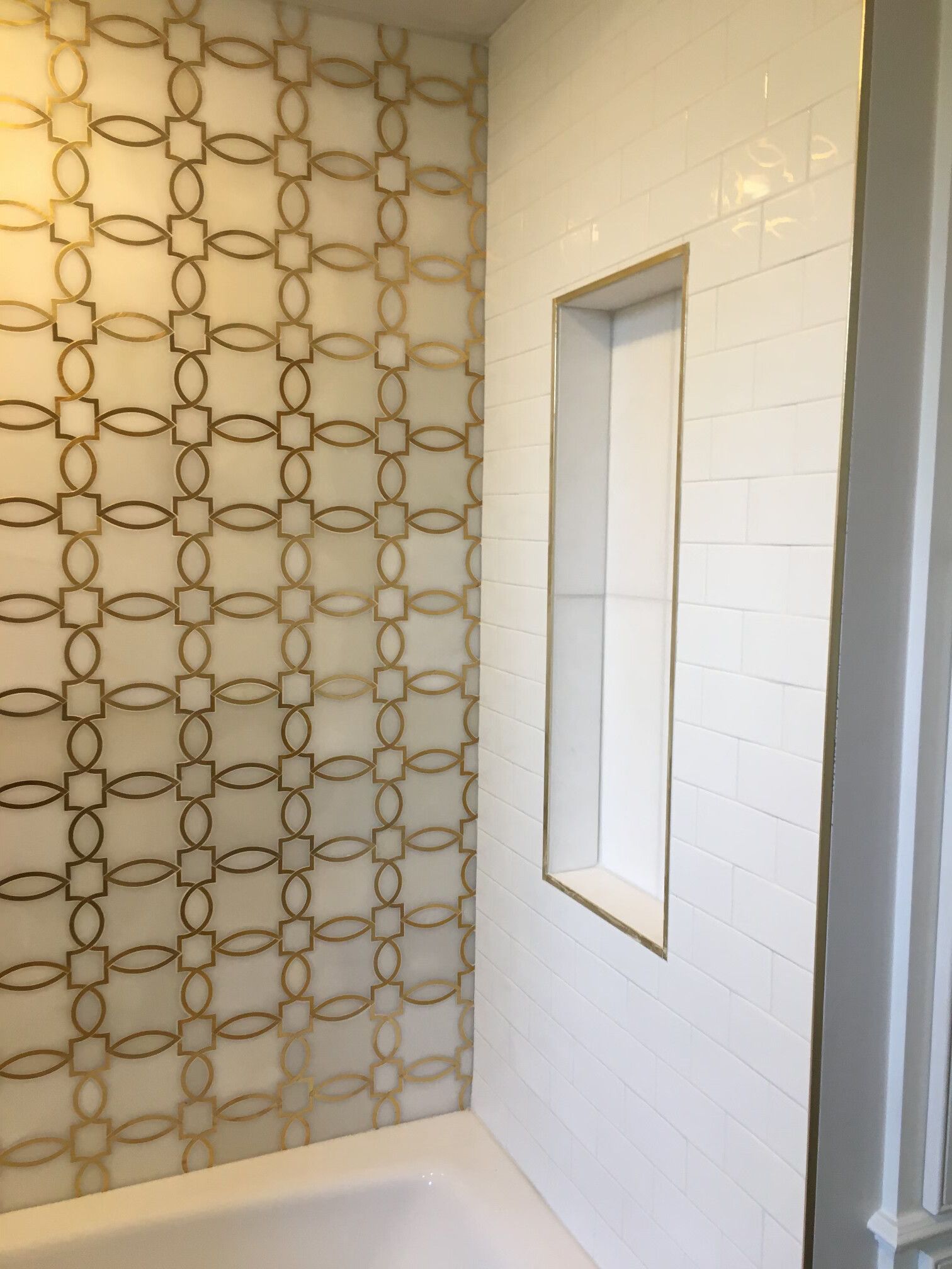 Shower with white subway tile and decorative gold tile accent wall; built-in niche with gold trim.