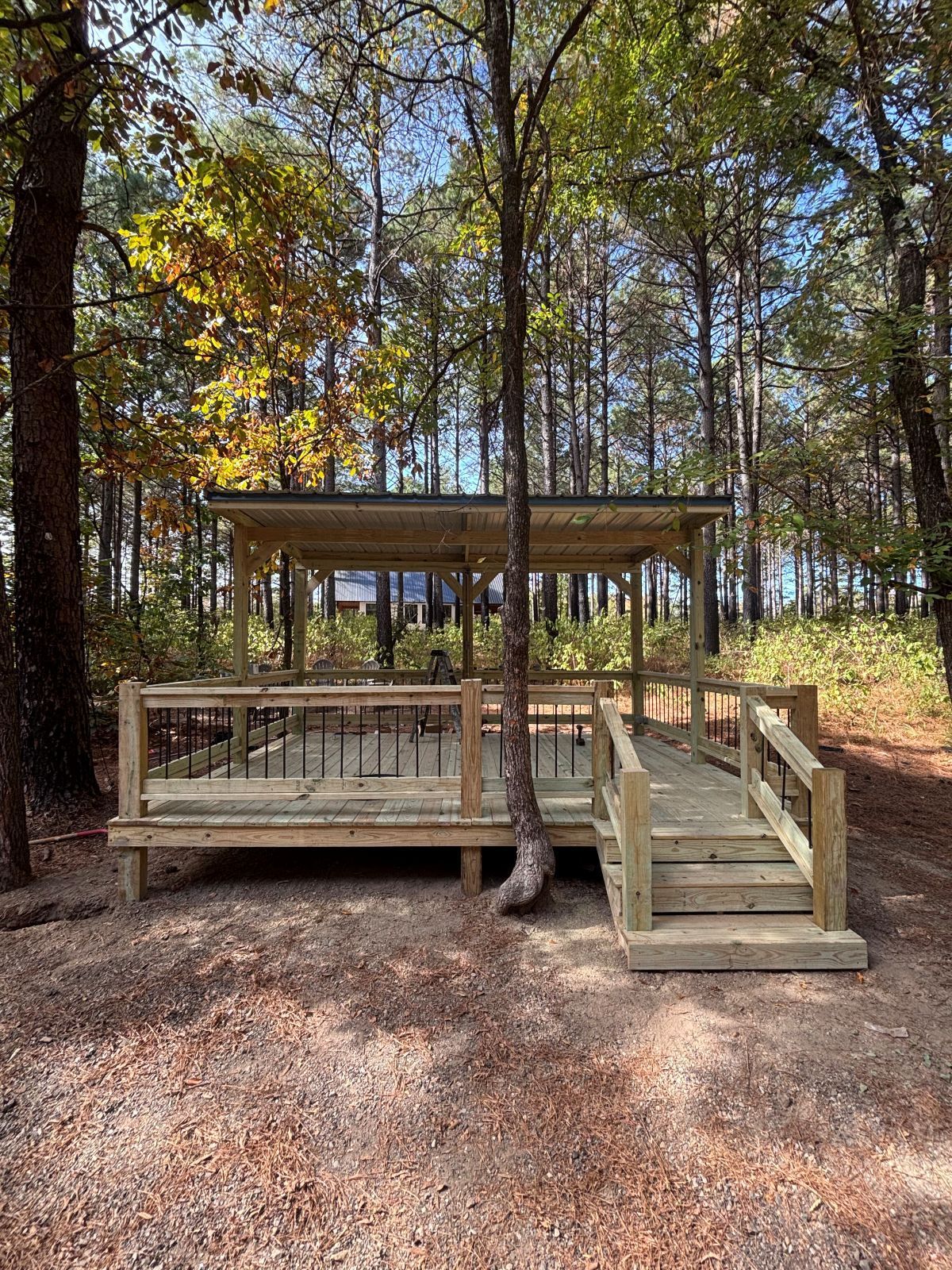 Wooden deck with a covered pavilion in a forest setting. A ramp provides accessibility.