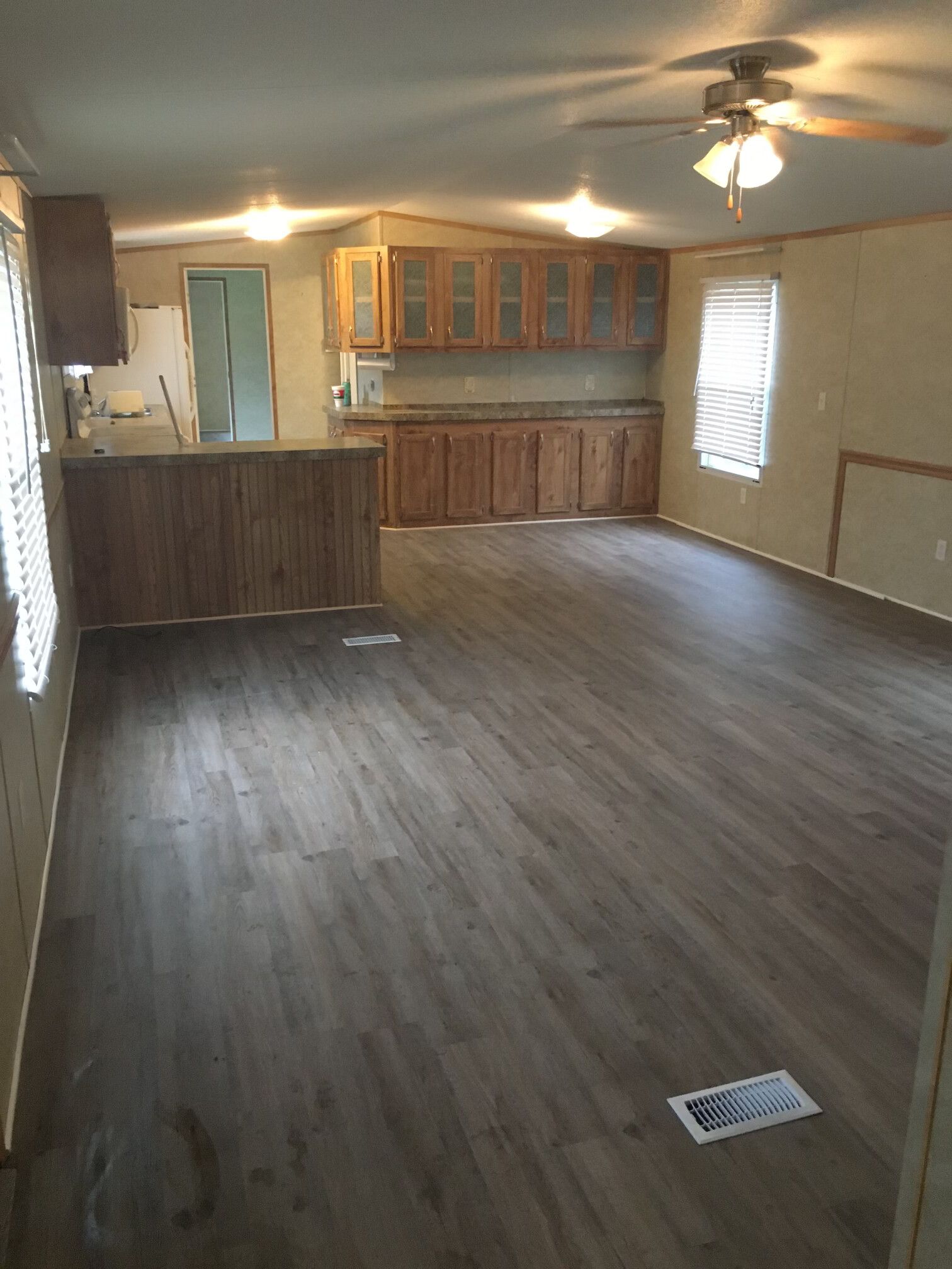 Open-plan living space with kitchen and wood-look flooring. Light wood cabinets, neutral walls, and a ceiling fan.