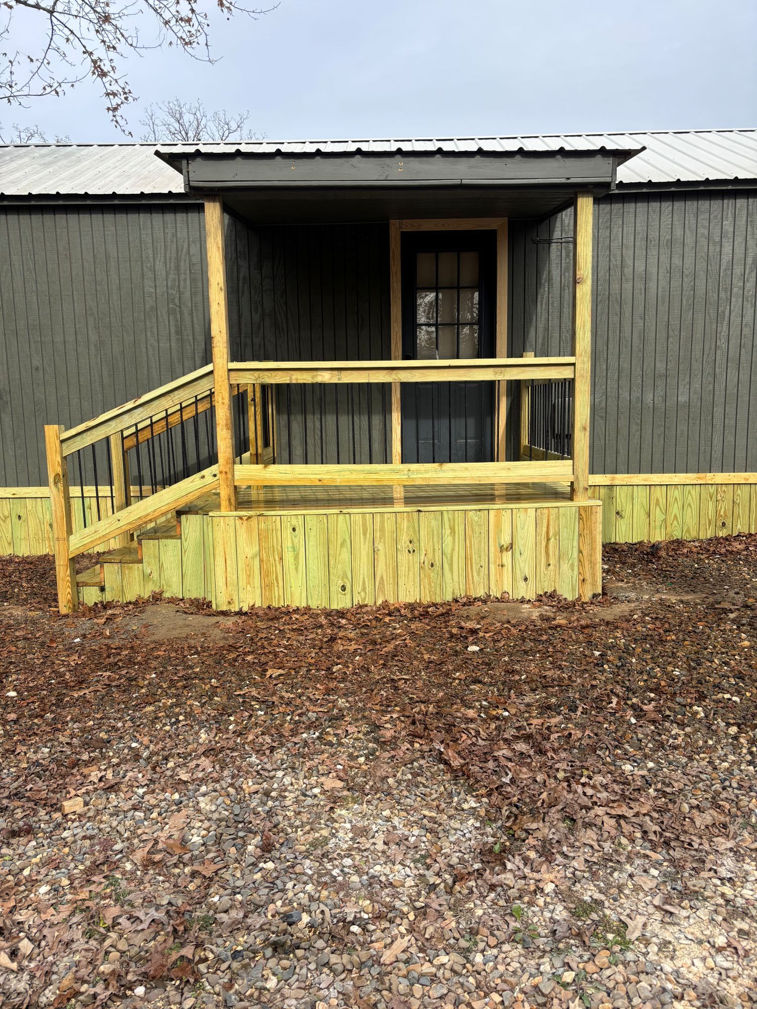 A dark-colored house with a newly-built wooden porch and stairs, set on a bed of brown leaves.