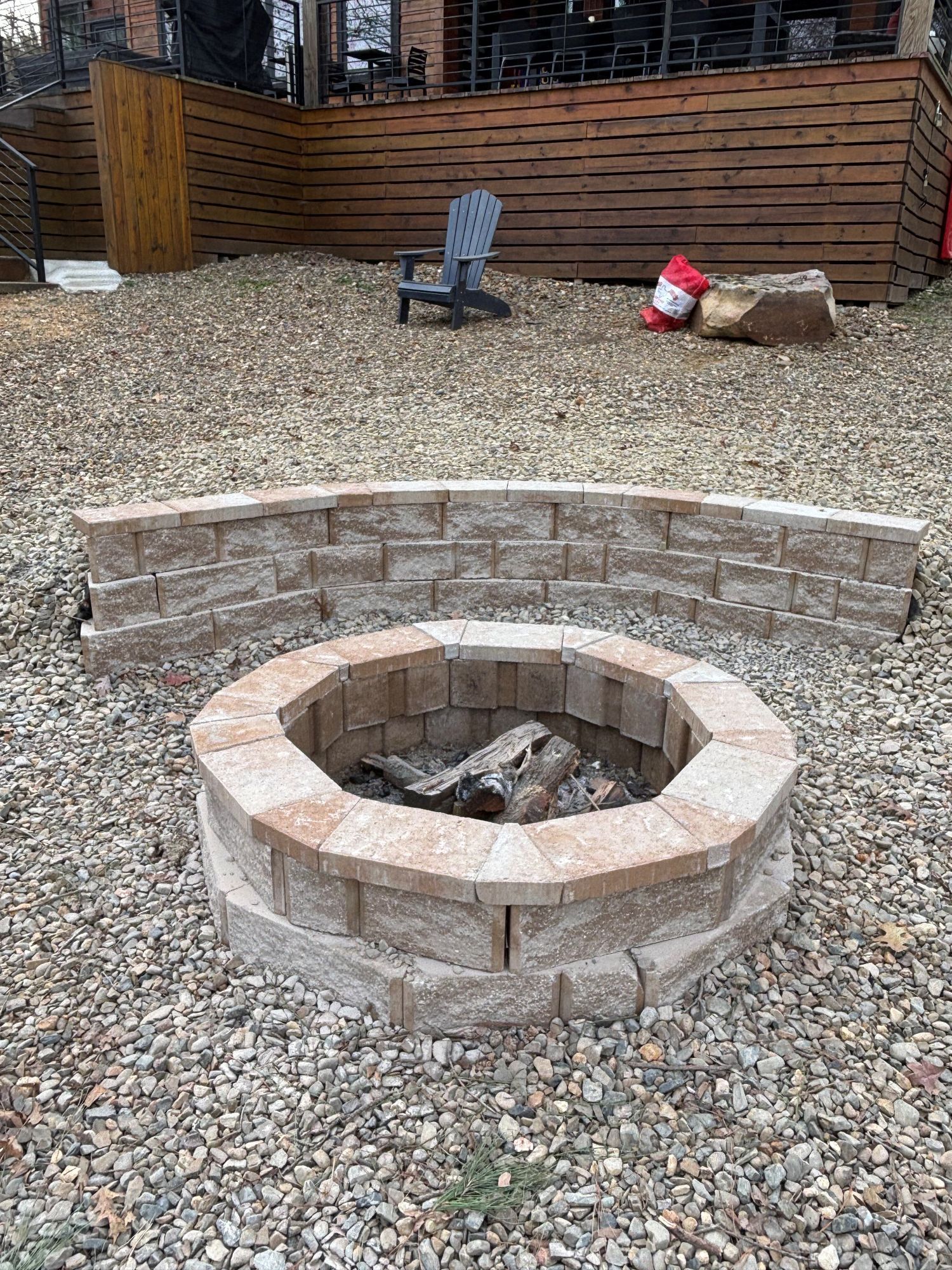 Stone fire pit with curved retaining wall on gravel in outdoor setting.