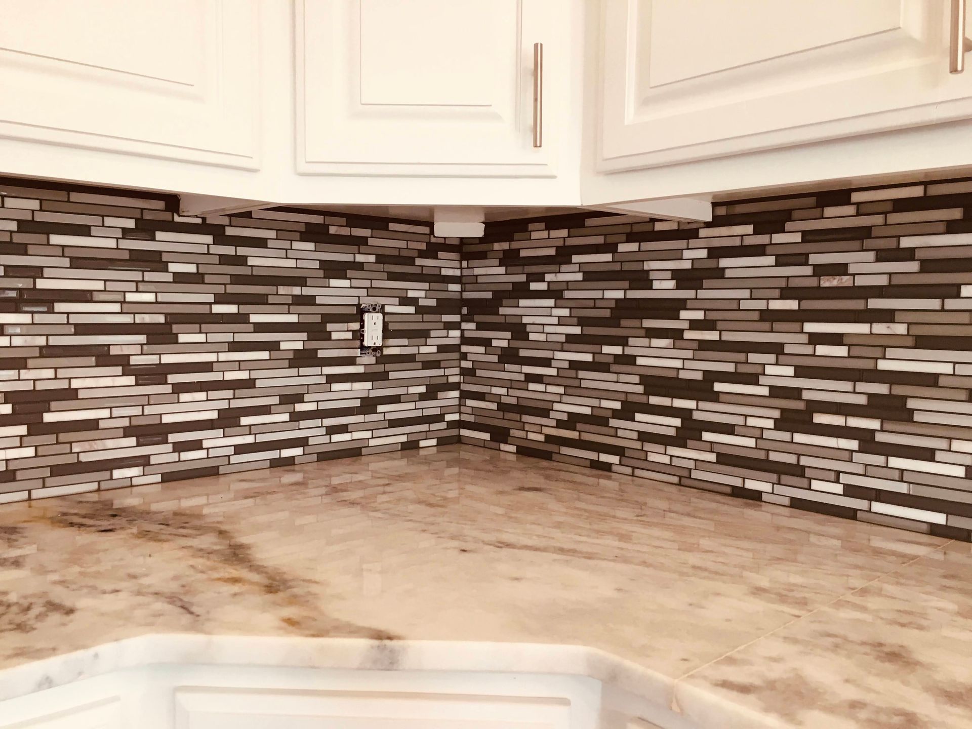 Kitchen corner with white cabinets, brown-beige countertop, and mosaic tile backsplash.