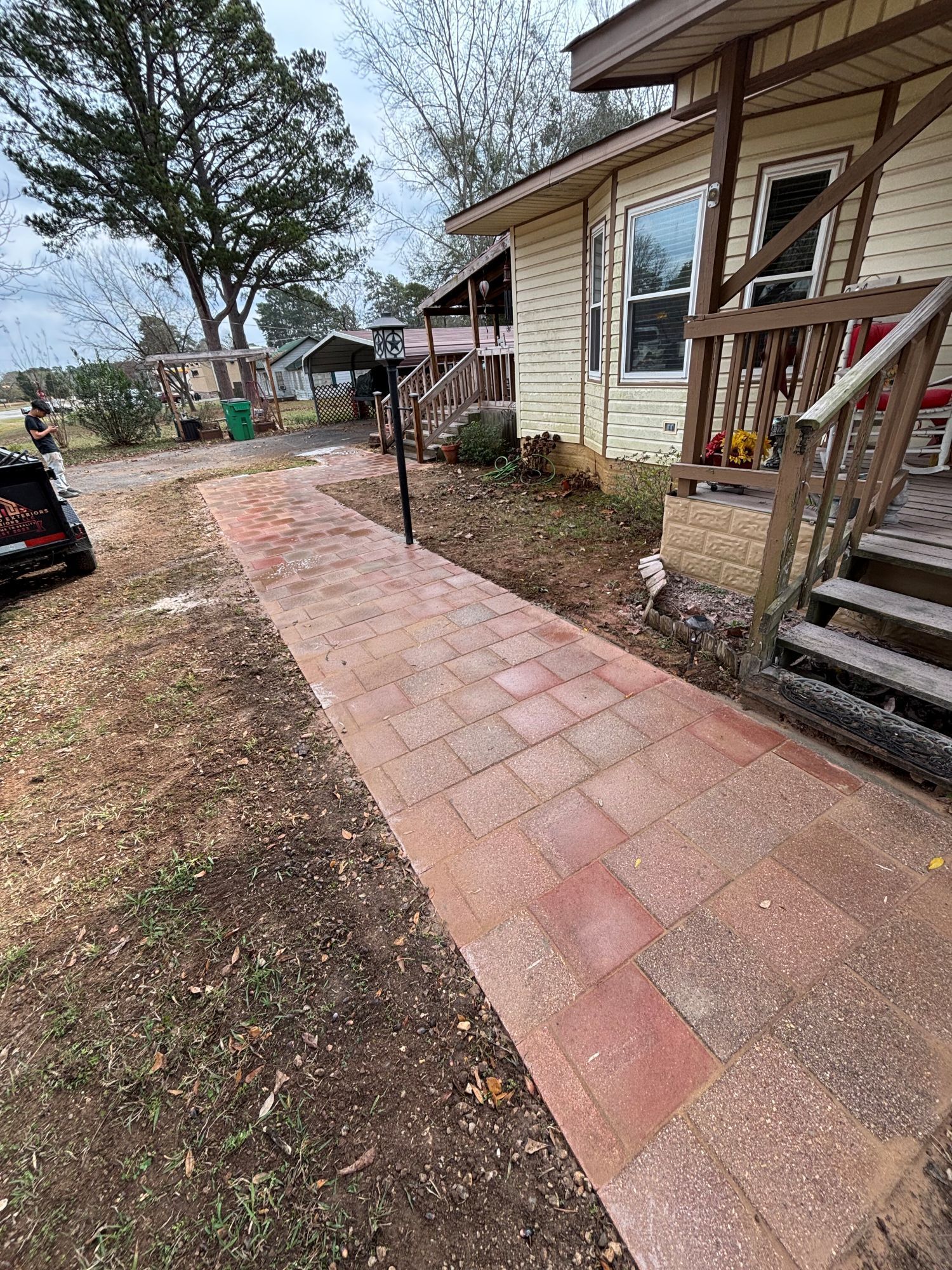 Brick walkway leading to a light-colored house with wooden stairs and a porch.