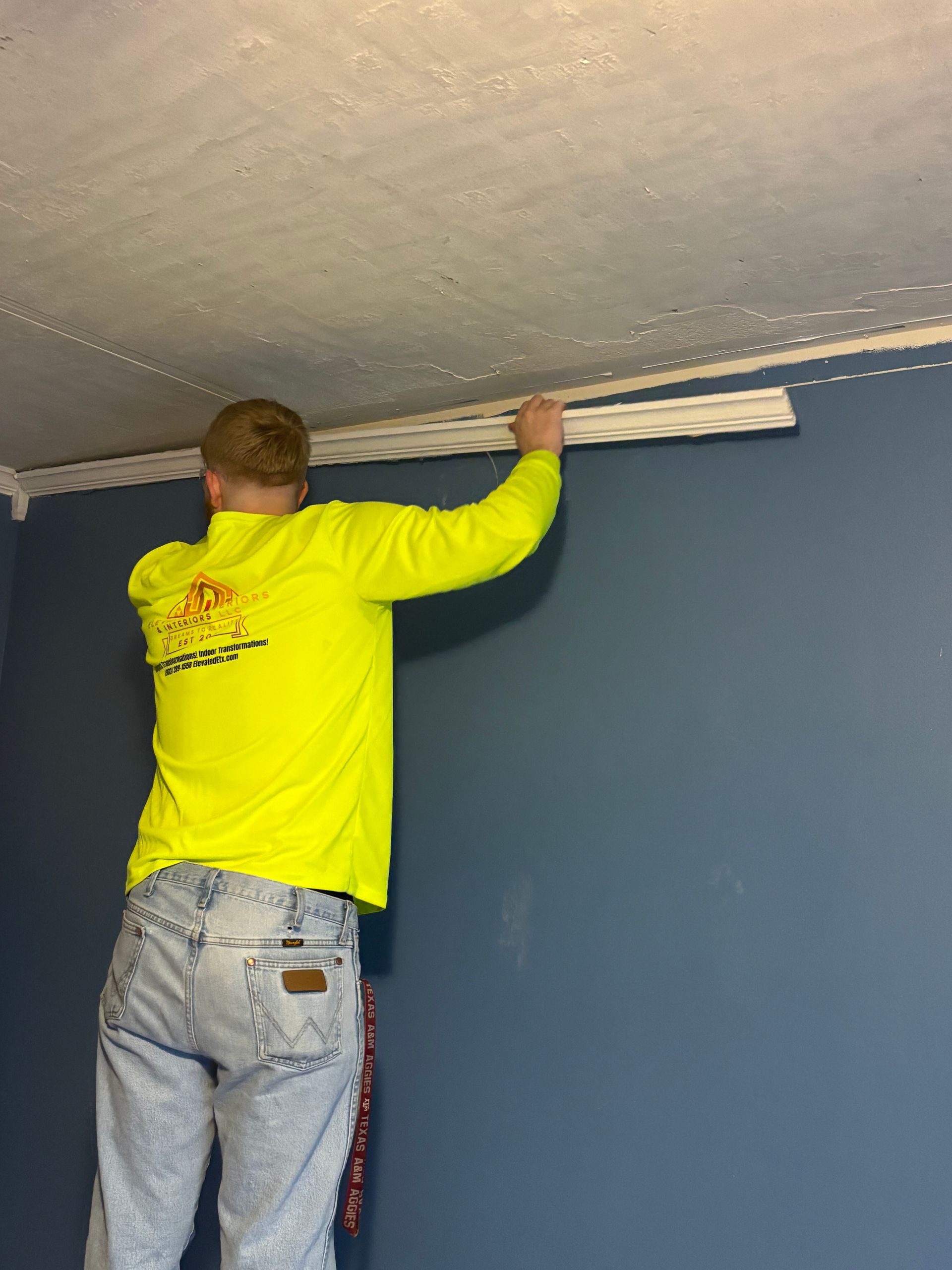 Person installing white trim on a blue wall, standing on a step stool.