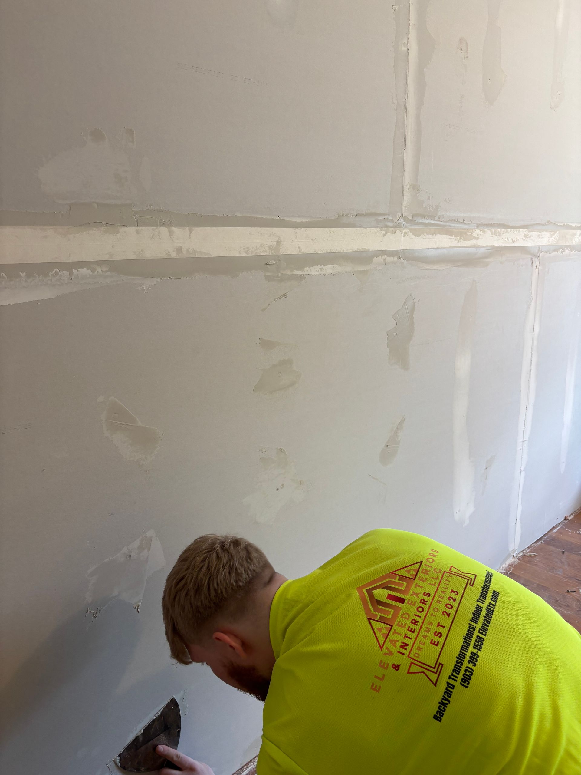 Person in yellow shirt smoothing drywall compound on a wall with a trowel.