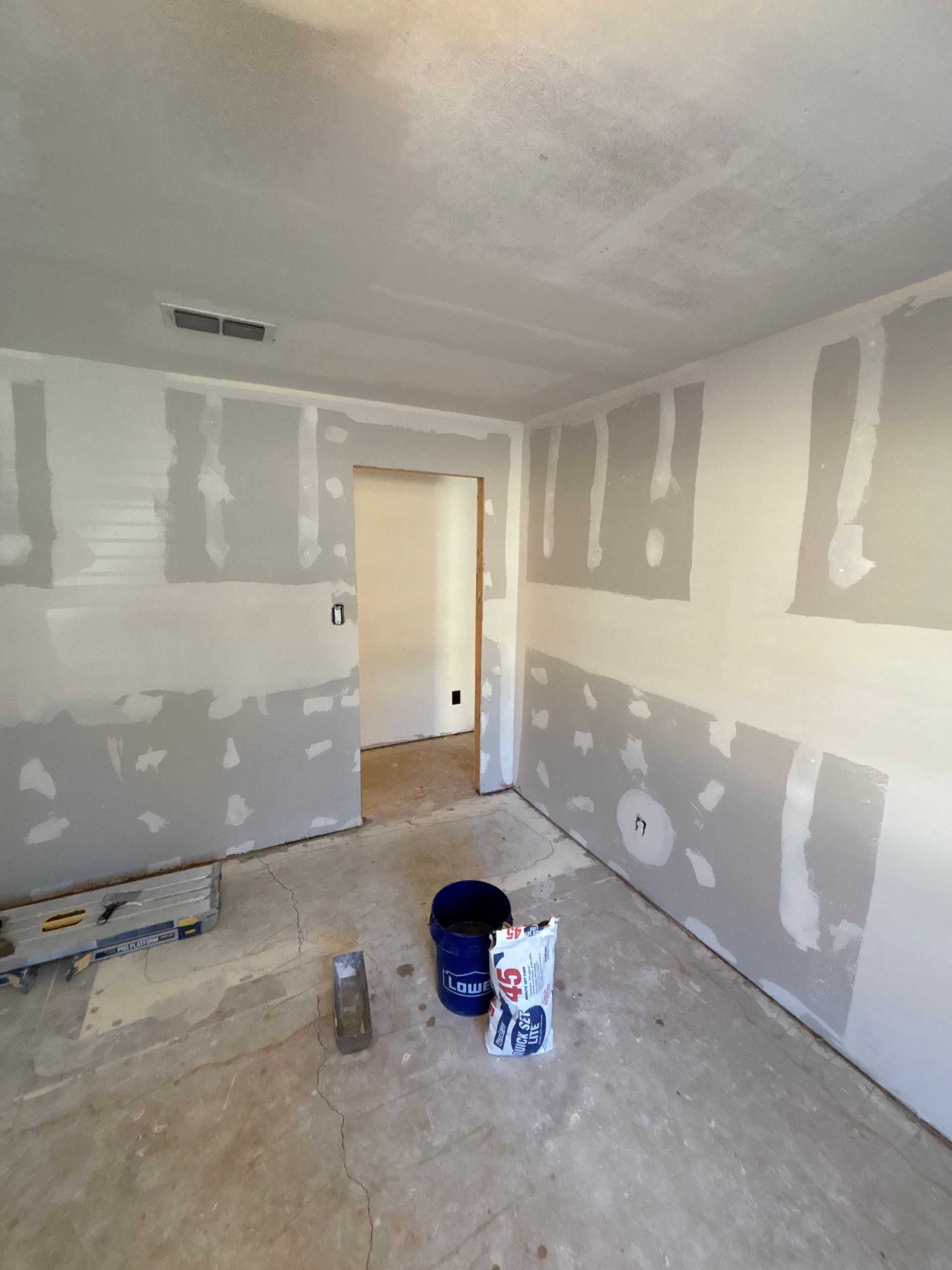 Room with drywall installed, mudded, and taped, with tools and materials on the floor.