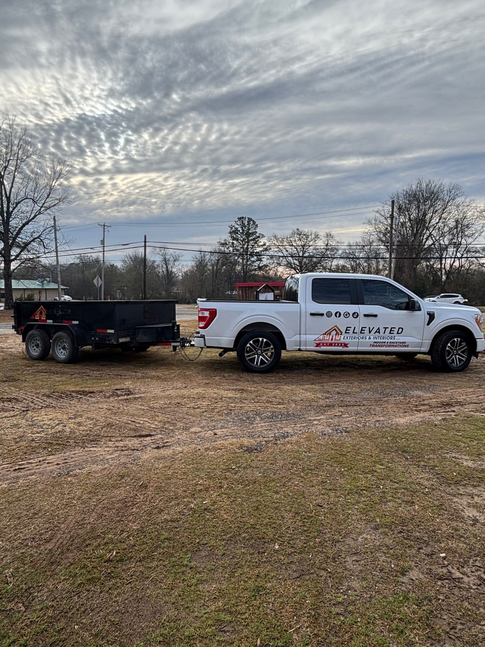 White pickup truck towing a black trailer on a cloudy day.