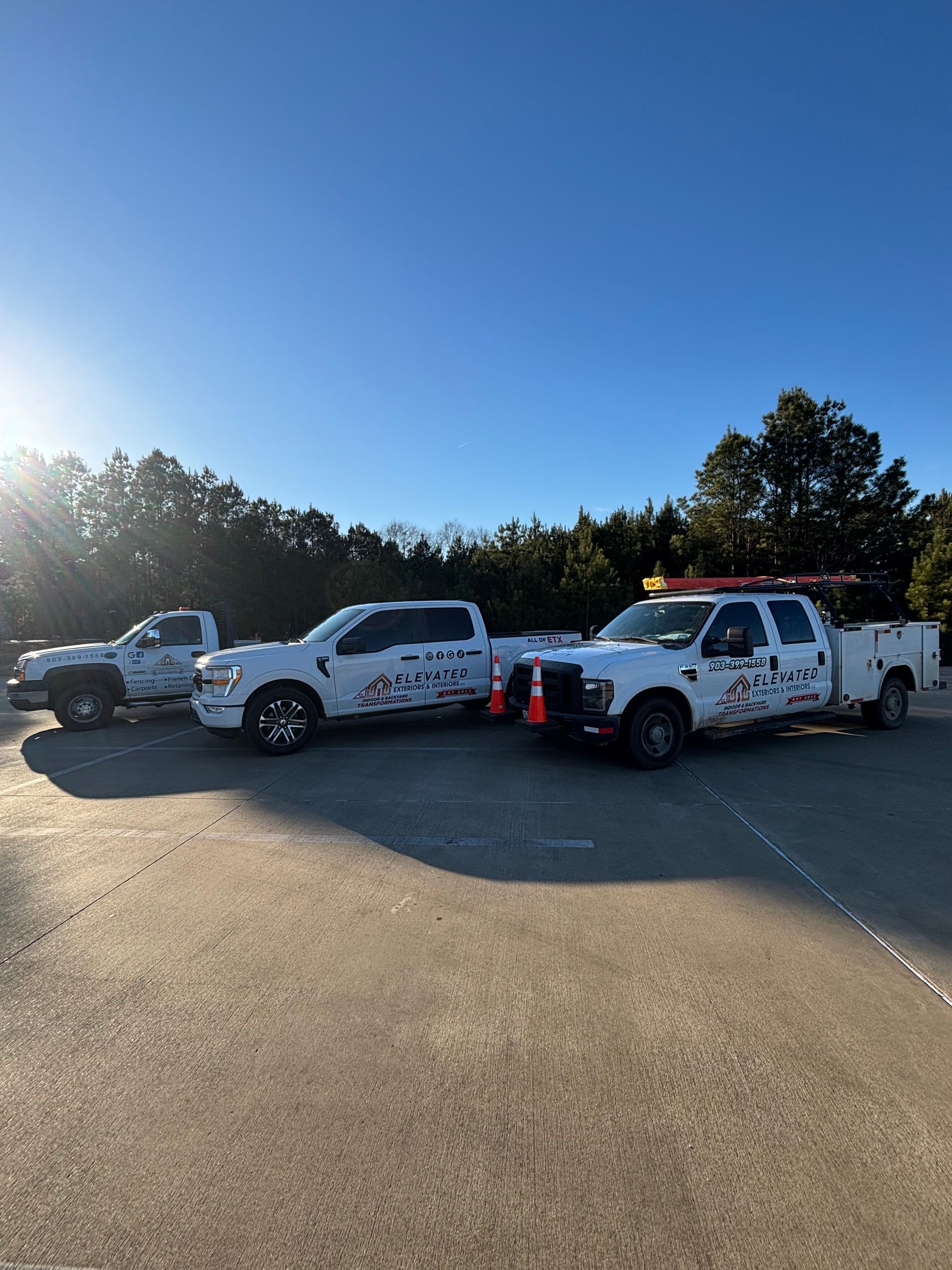 Three white work trucks parked on a paved surface on a sunny day.