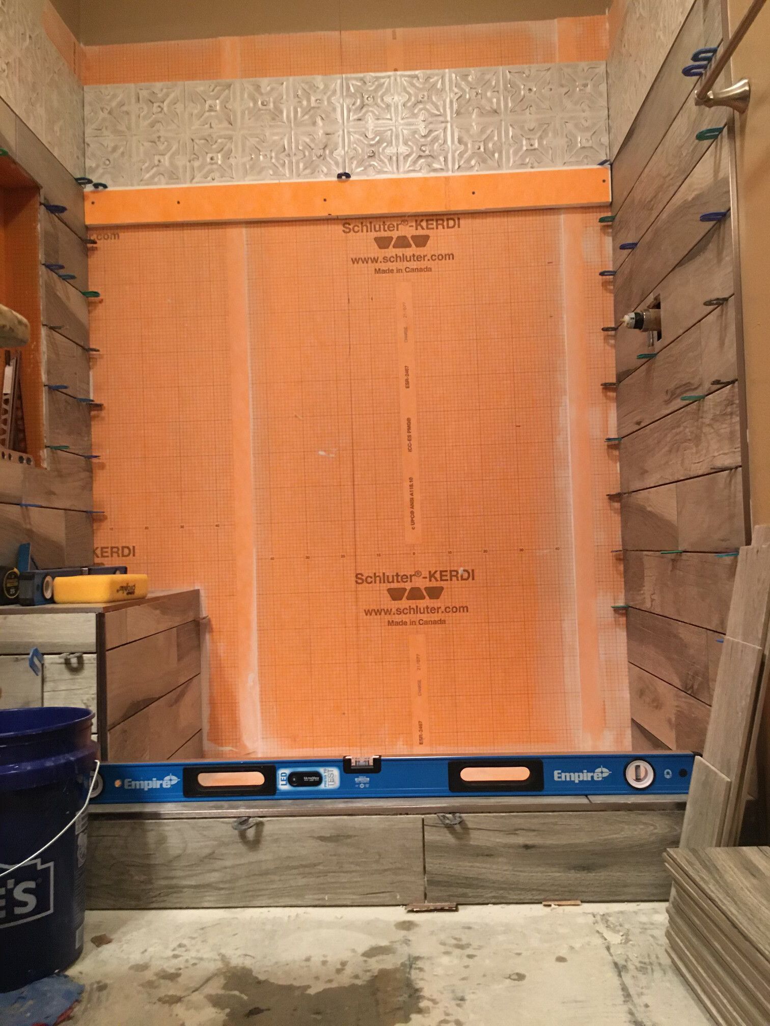 Shower under construction with orange waterproof membrane. Tile installed on side walls, level on base.