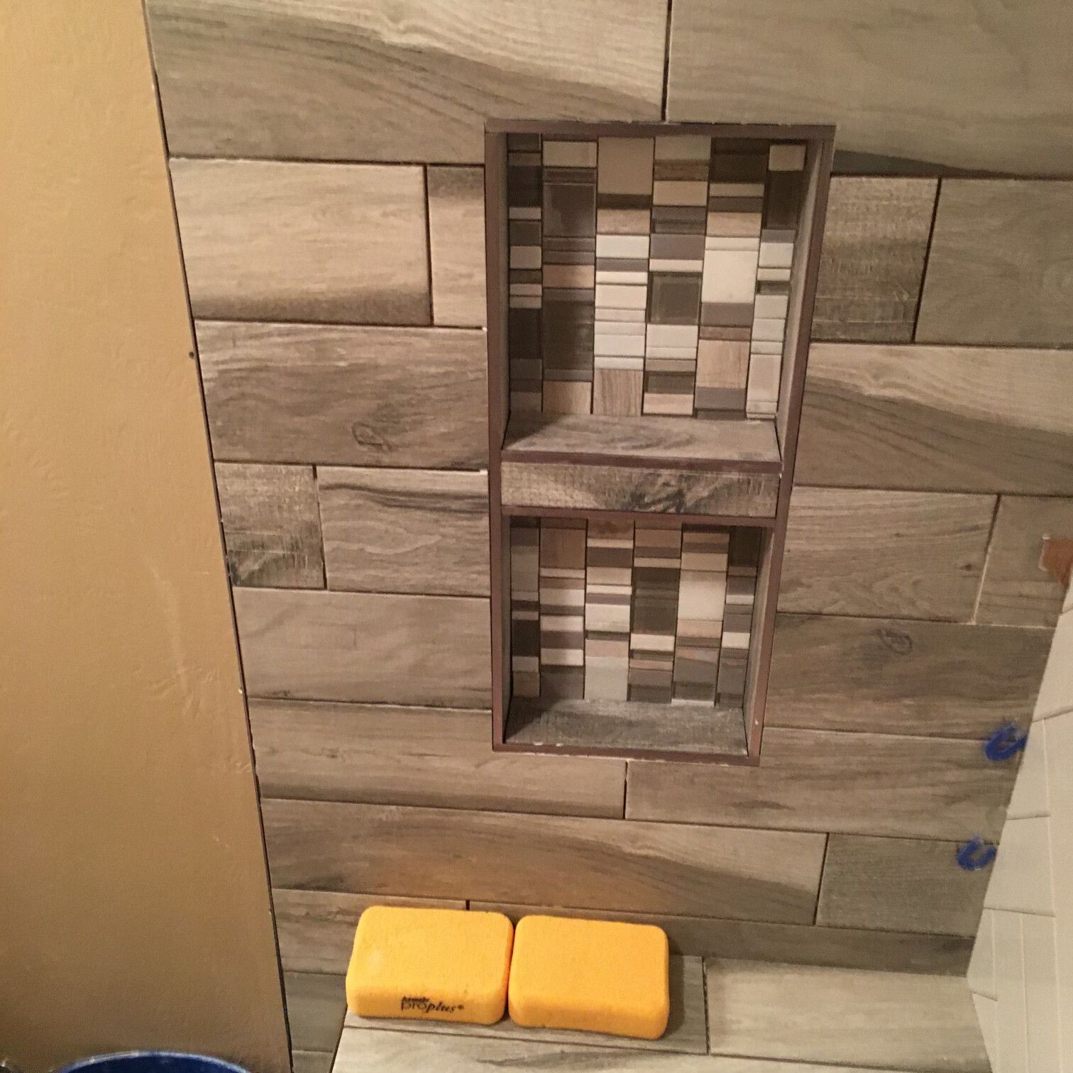 Shower wall with built-in shelf. Gray, rectangular tiles with a patterned shelf interior. Two yellow bars of soap sit below.