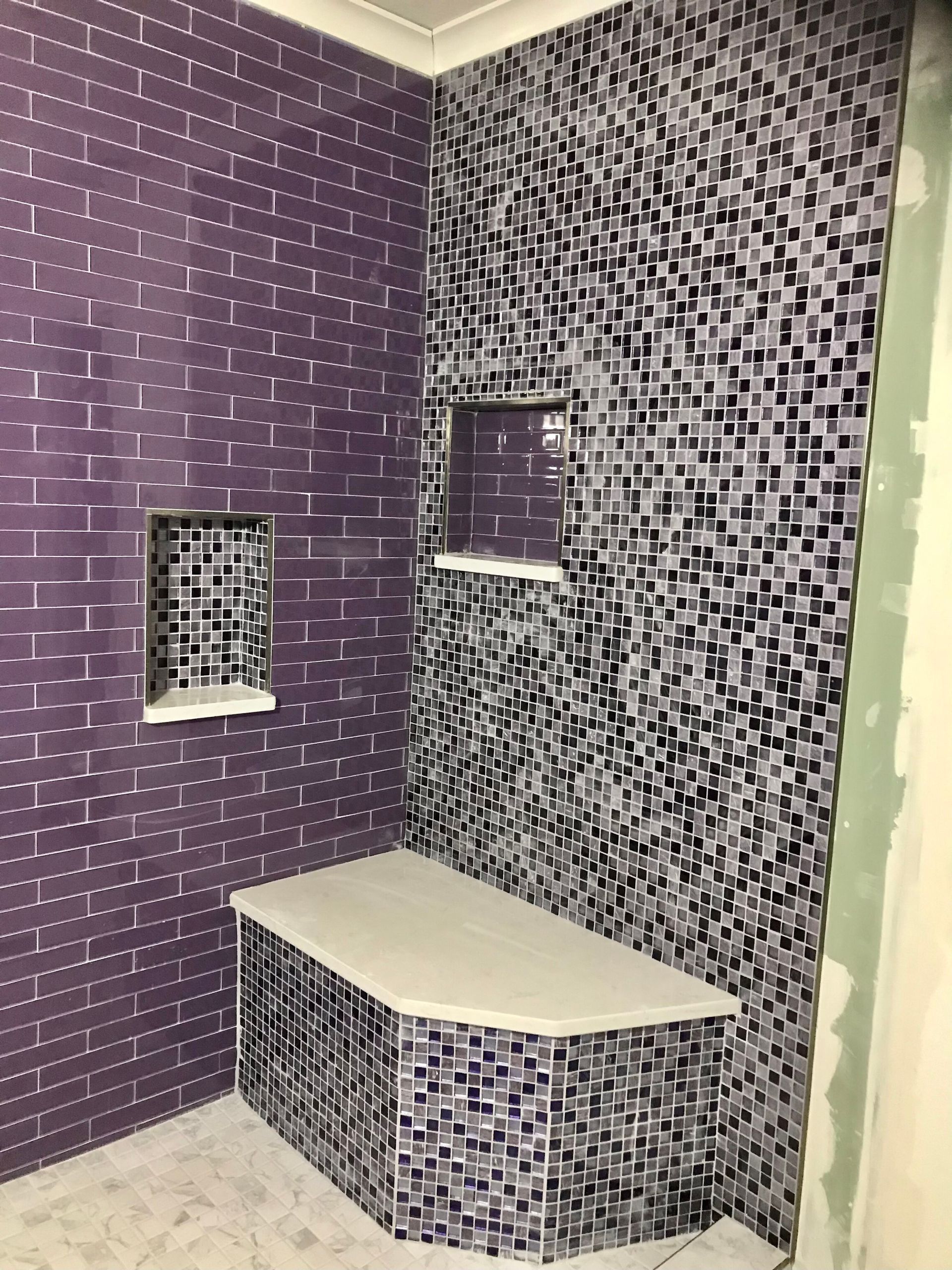 Purple and black mosaic tile shower with built-in bench and shelves.