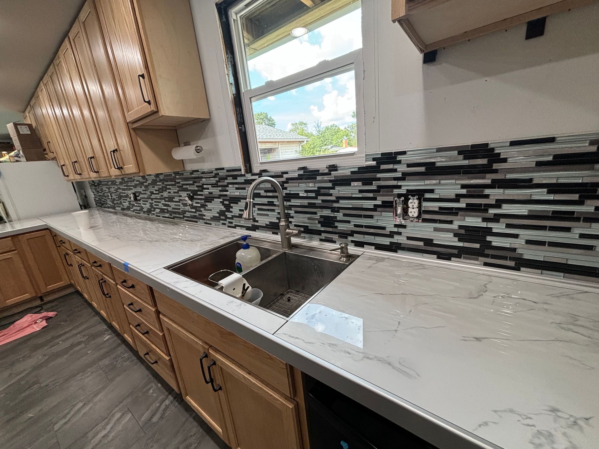 Kitchen with light-colored cabinets, stainless steel sink, white countertops, and a black and white tiled backsplash.