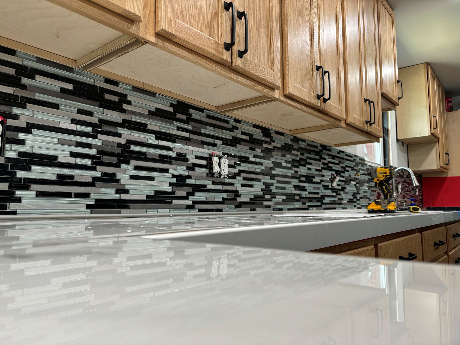 Kitchen with light-colored cabinets, white countertop, and mosaic tile backsplash; tools and outlet visible.