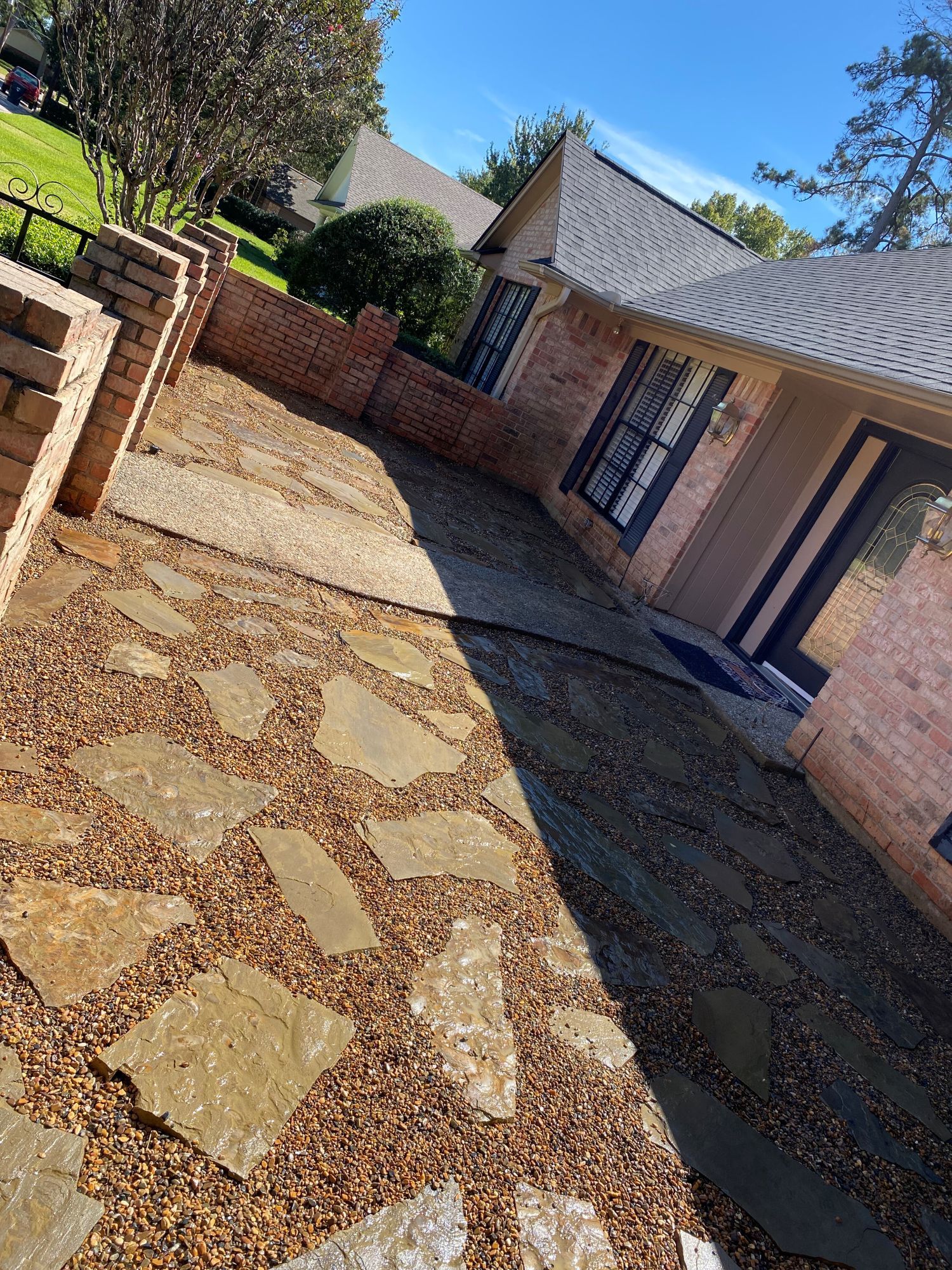 Stone pathway with small gravel and brick wall leading to a house with black shutters and a dark door.