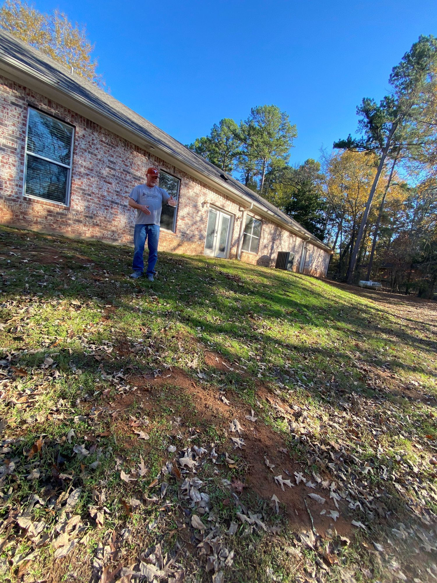 Man standing on a grassy hill in front of a brick building. Bright blue sky.