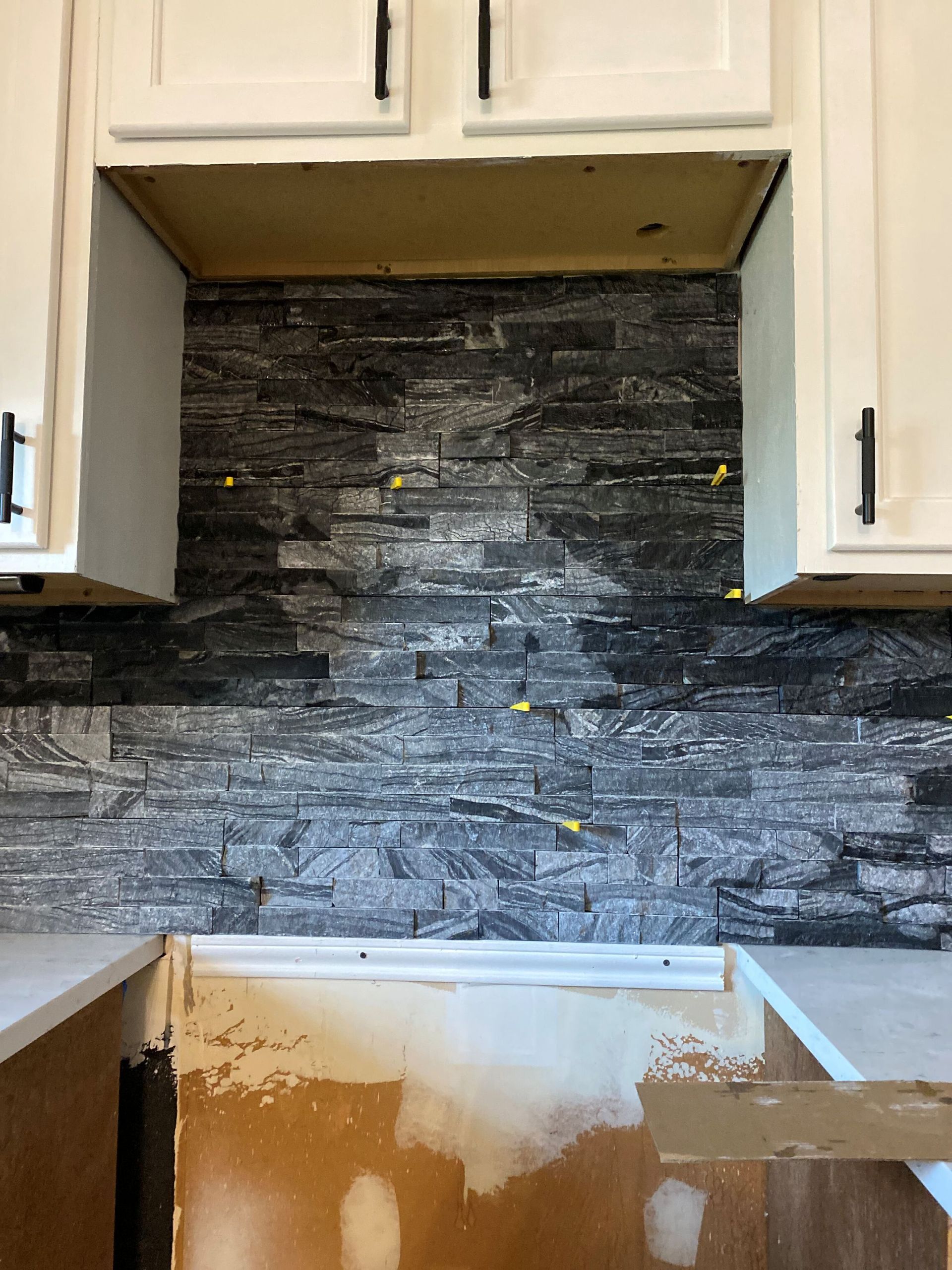 Gray stone tile backsplash installed in a kitchen, between white cabinets.