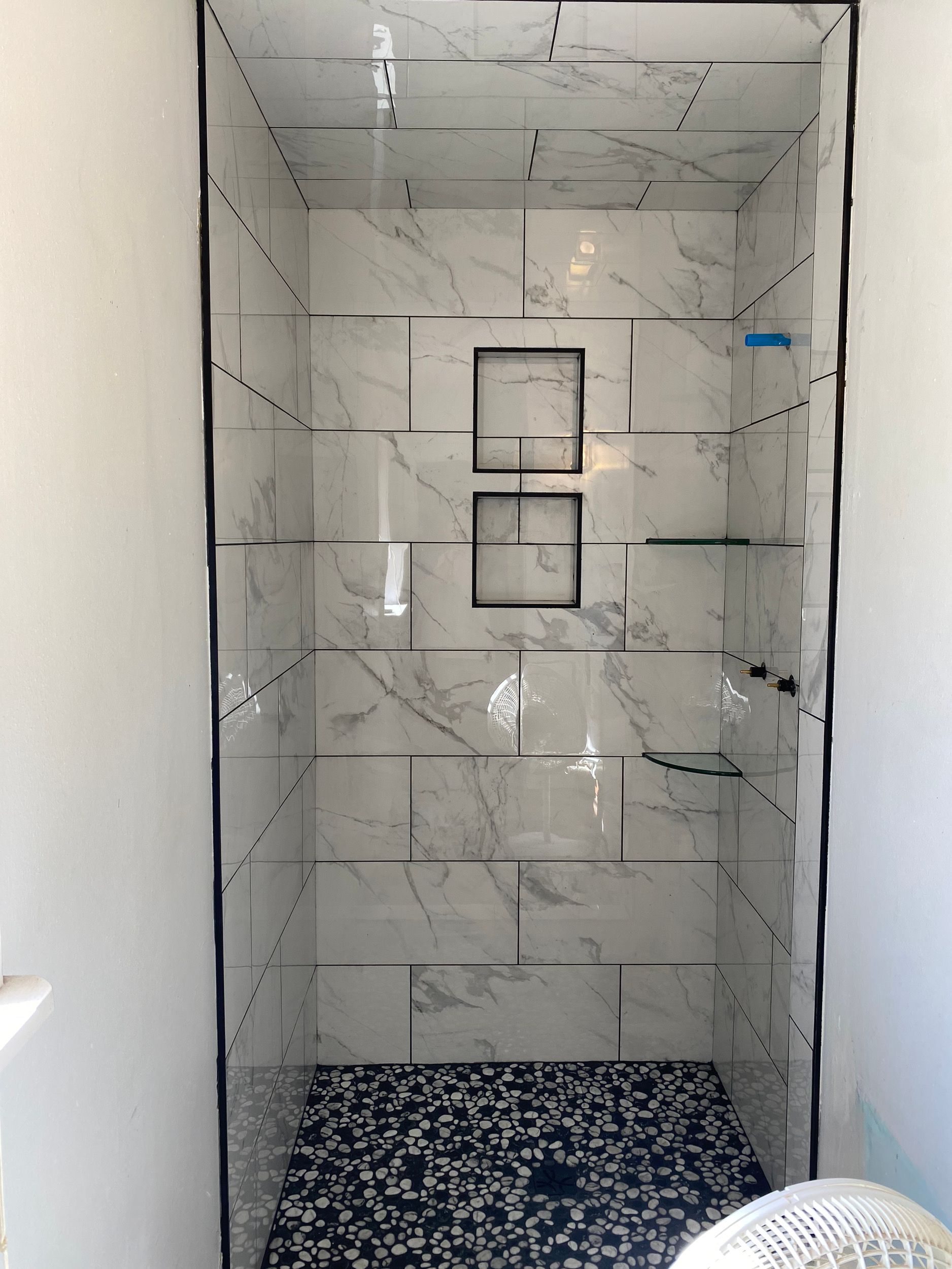 Tiled shower with marble-look walls, mosaic floor, two square inset shelves, and black grout.