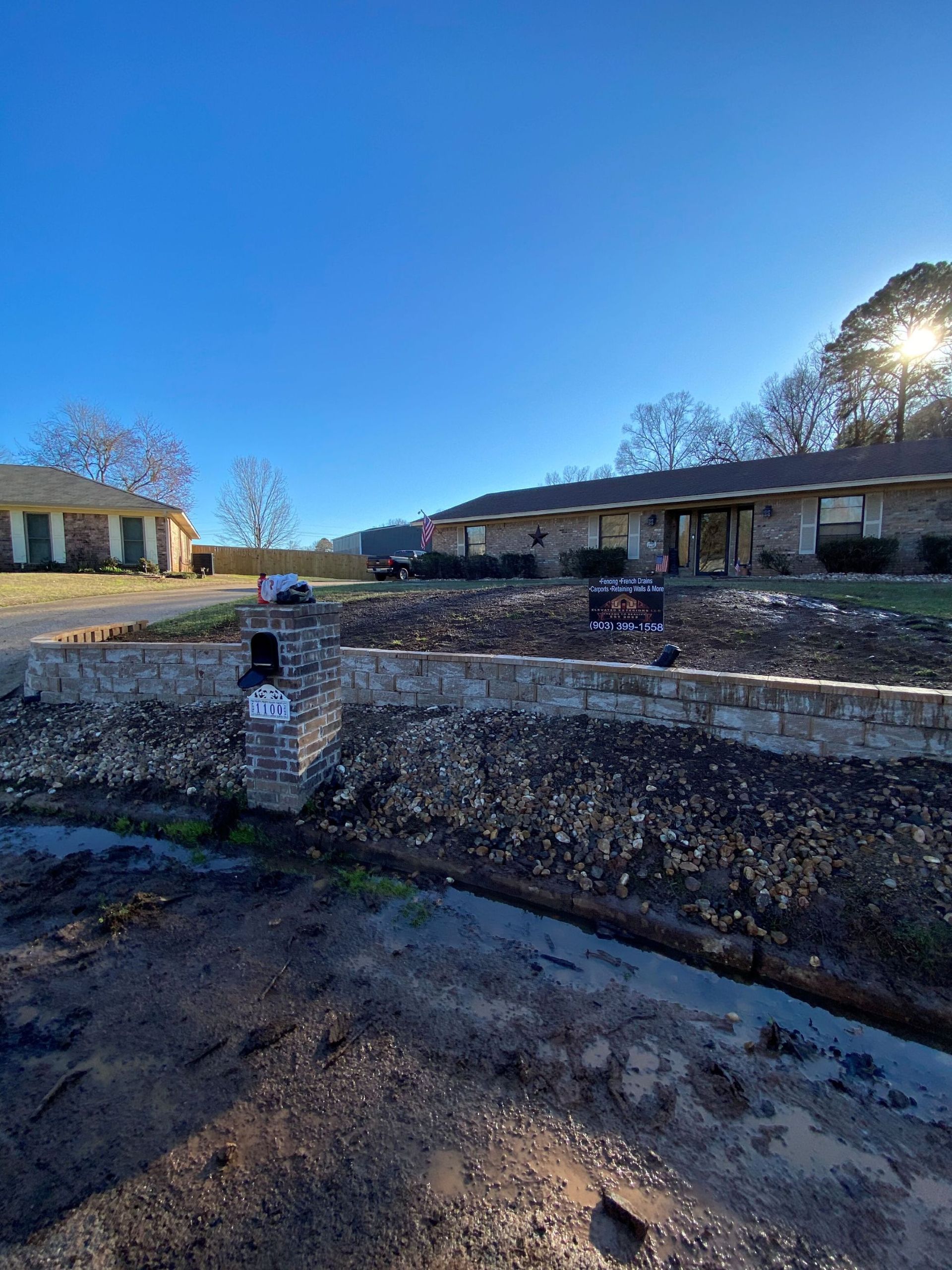 Stone retaining wall and mailbox in front of a house. Sunlight shines from the right.