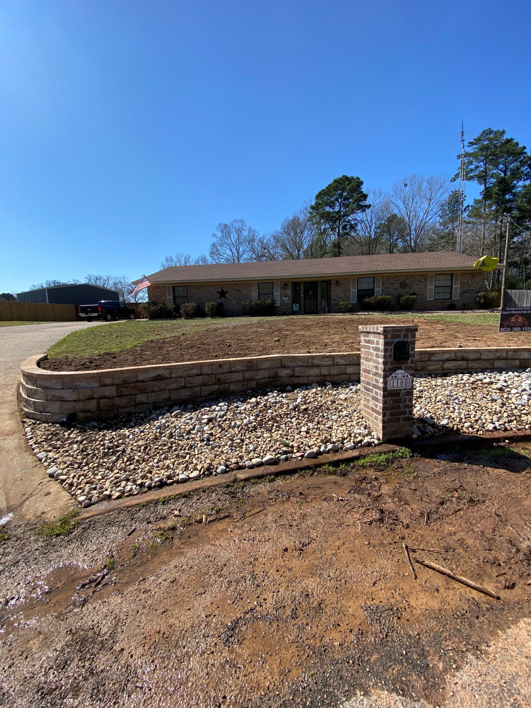 House with rock retaining walls, brown dirt, and blue sky.