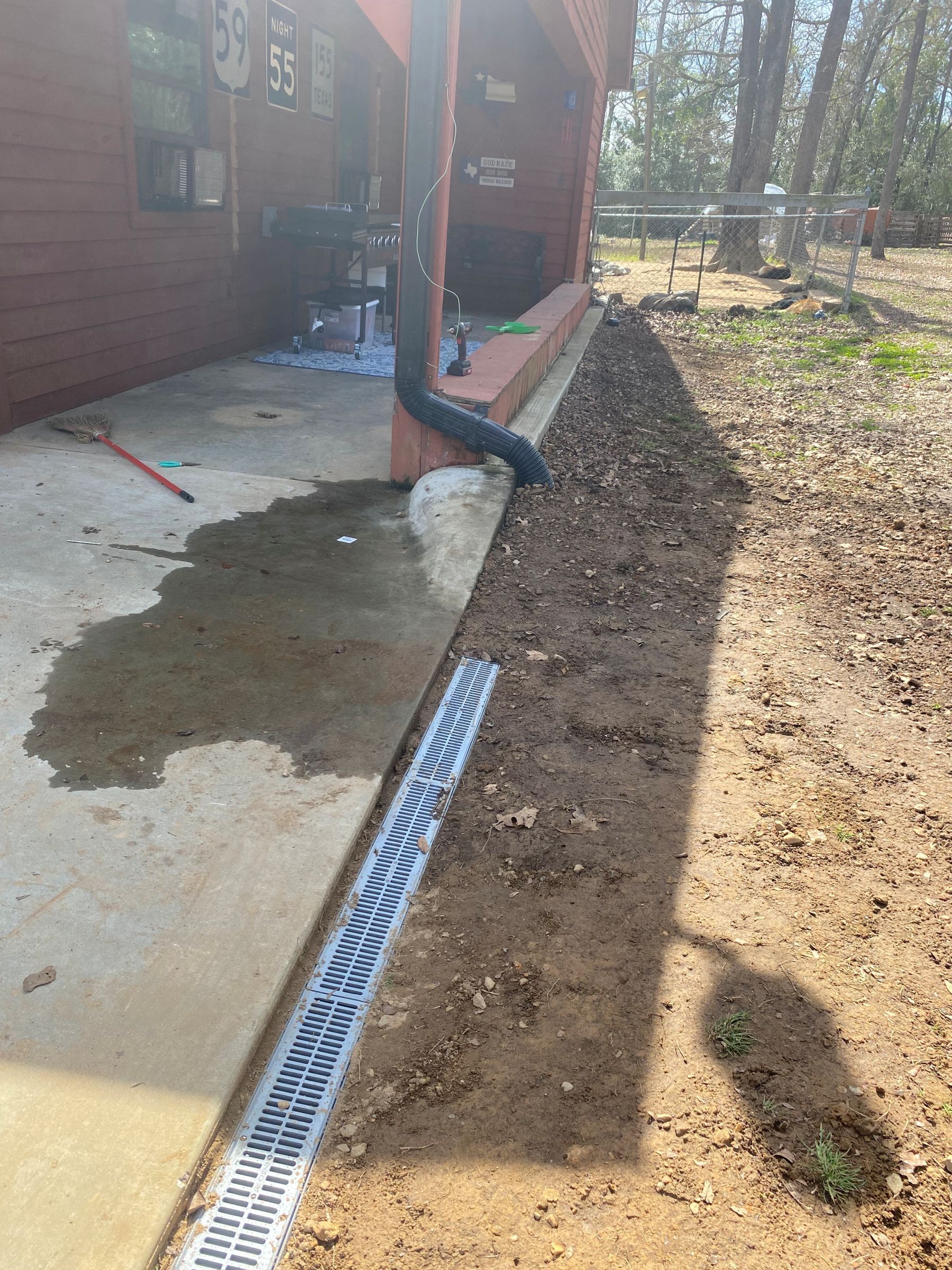 A gutter directs water into a linear drain on a concrete patio next to a house with exposed wood siding.