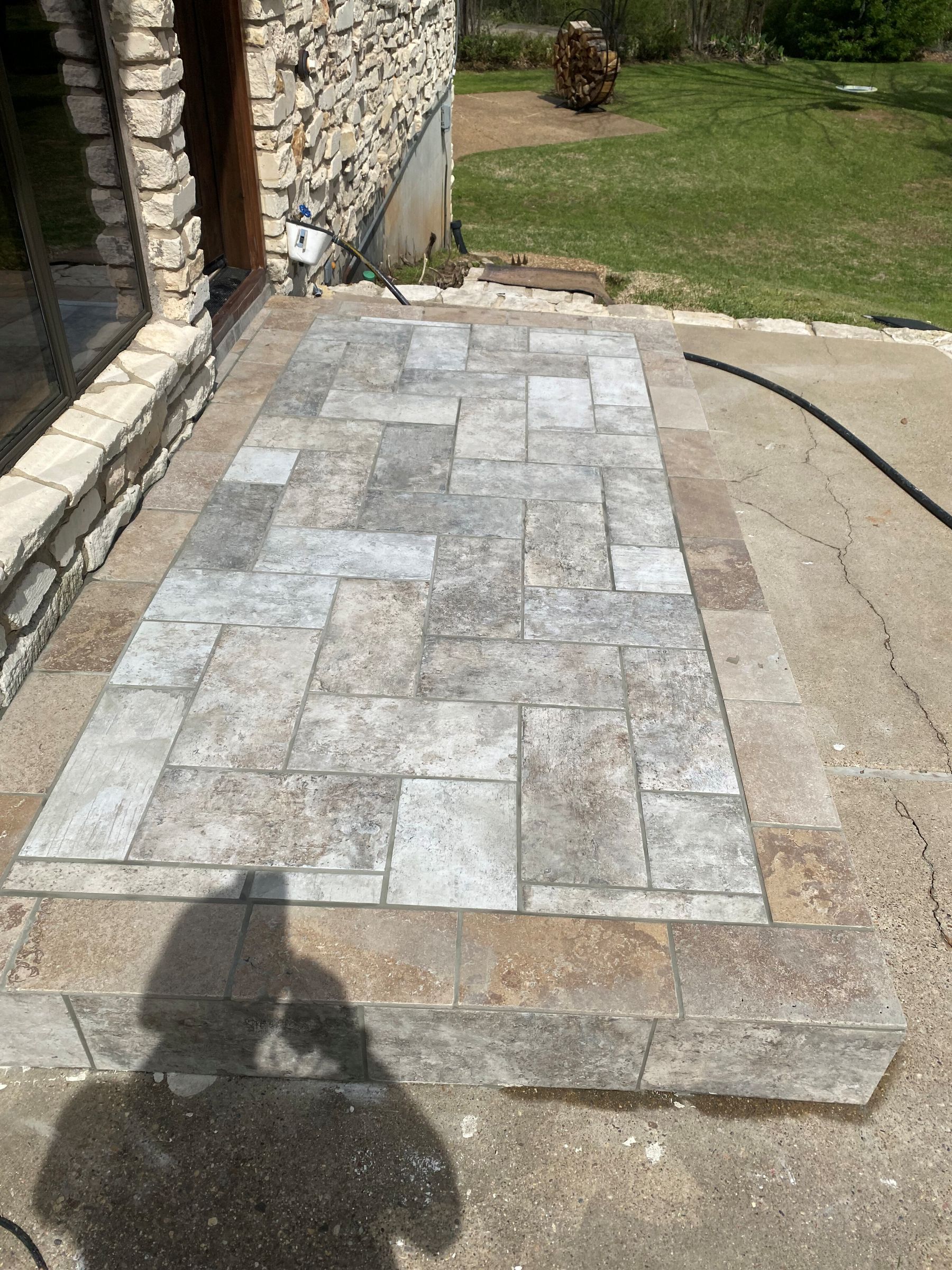 Patio with stone pavers and steps, near a stone building and grass. Shadow of person visible.