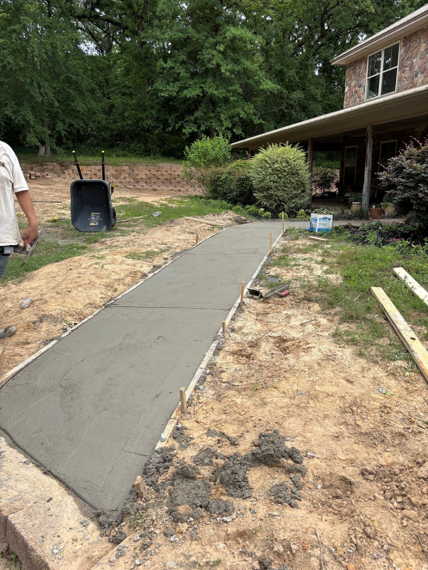 Freshly poured concrete walkway next to a house with a brick facade.