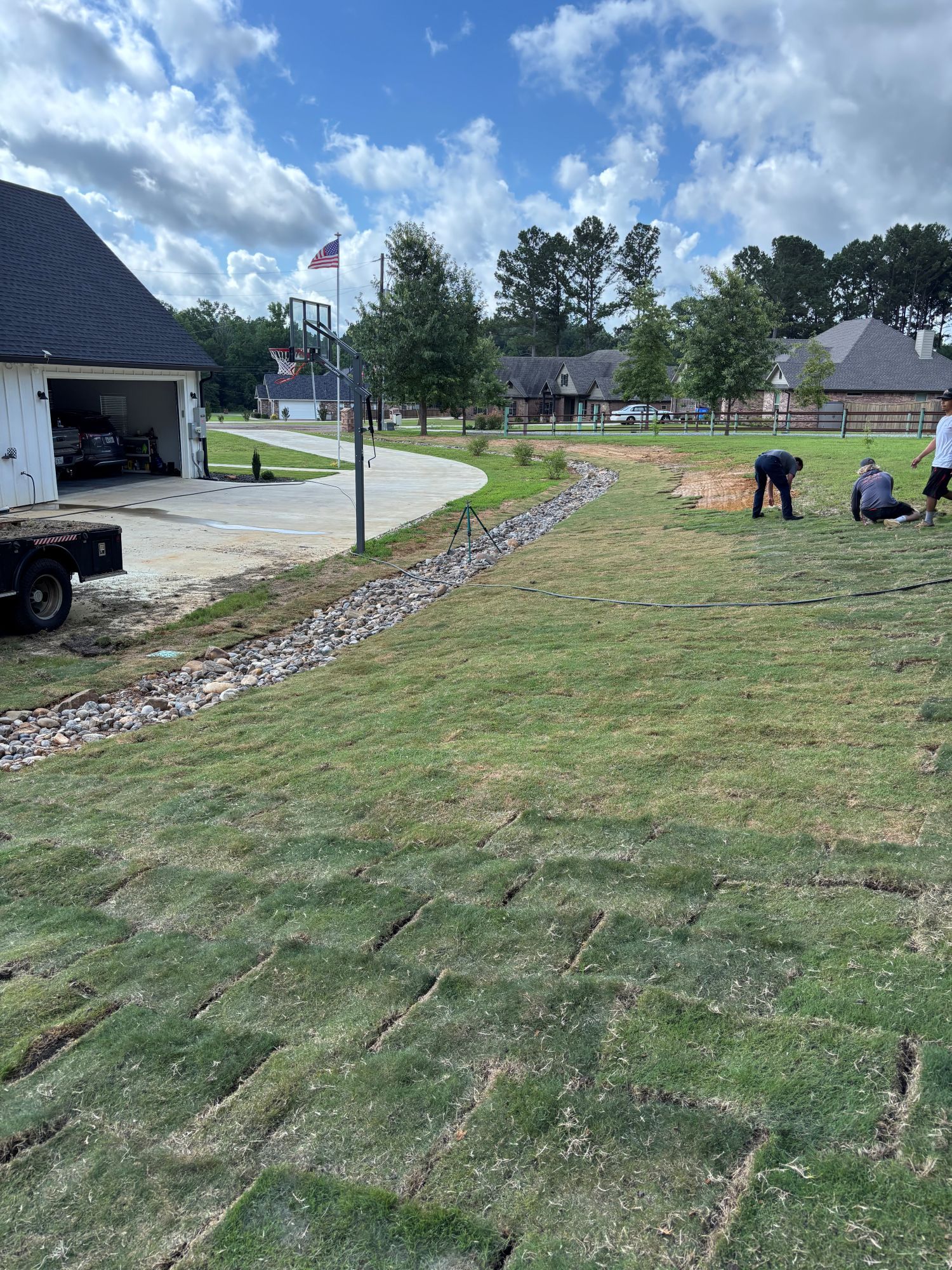 Laying sod in a yard; workers, driveway, rocks, and a flag.