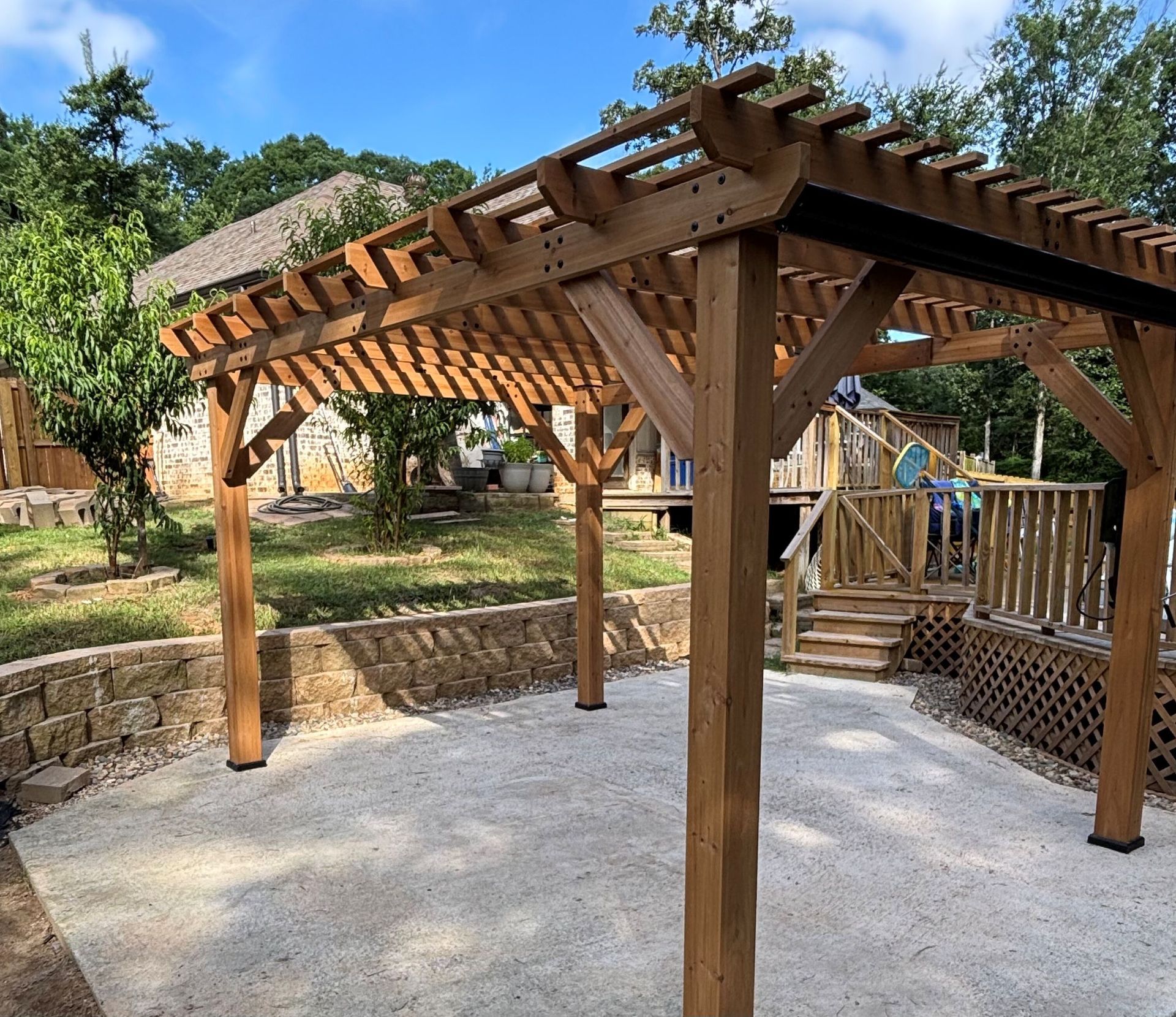 Wooden pergola over a gravel patio, with a stone wall and deck in the background.