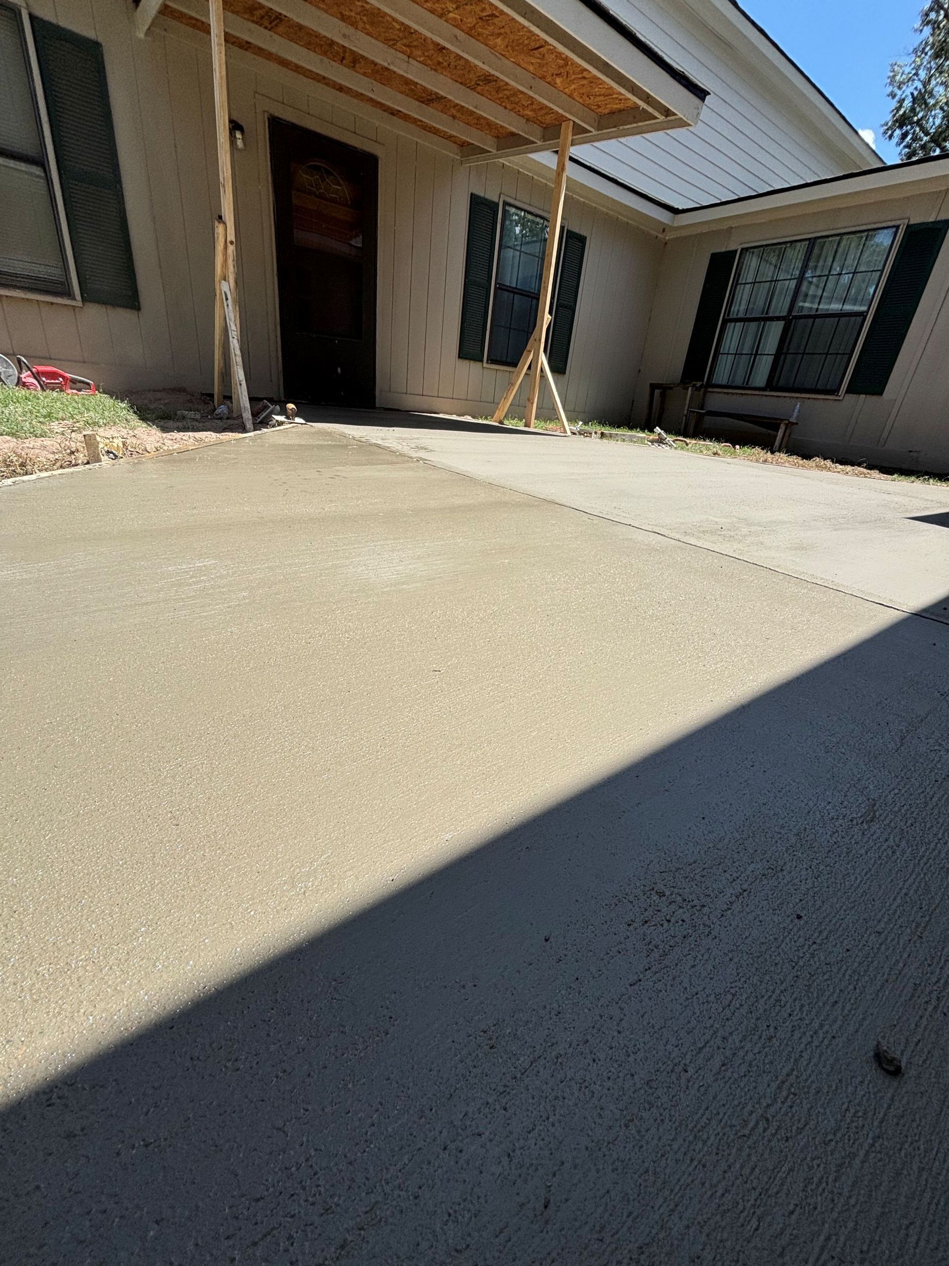 Concrete driveway leading to a house with a covered entrance and shuttered windows.