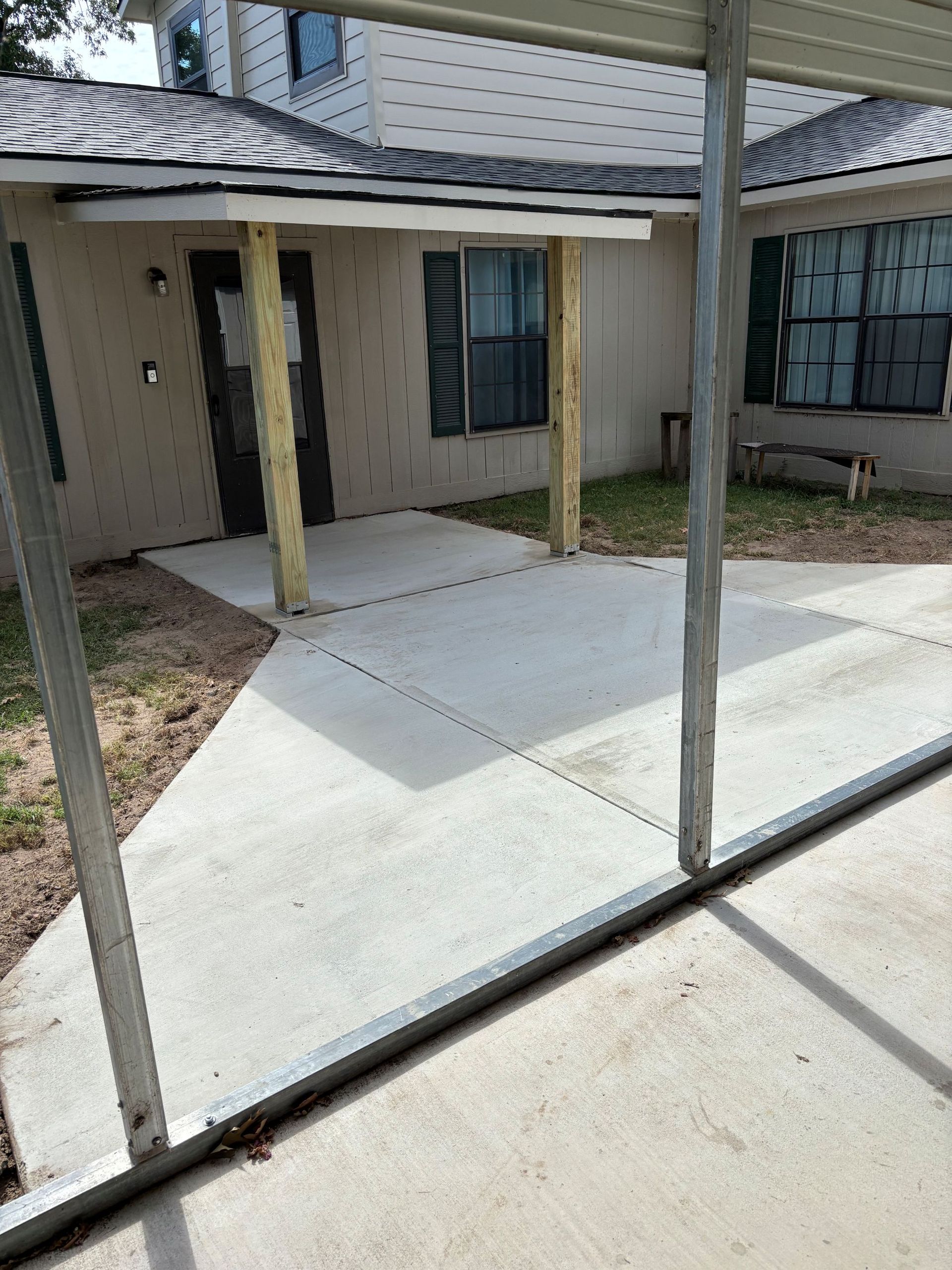 Concrete patio leading to a house with a carport in view.