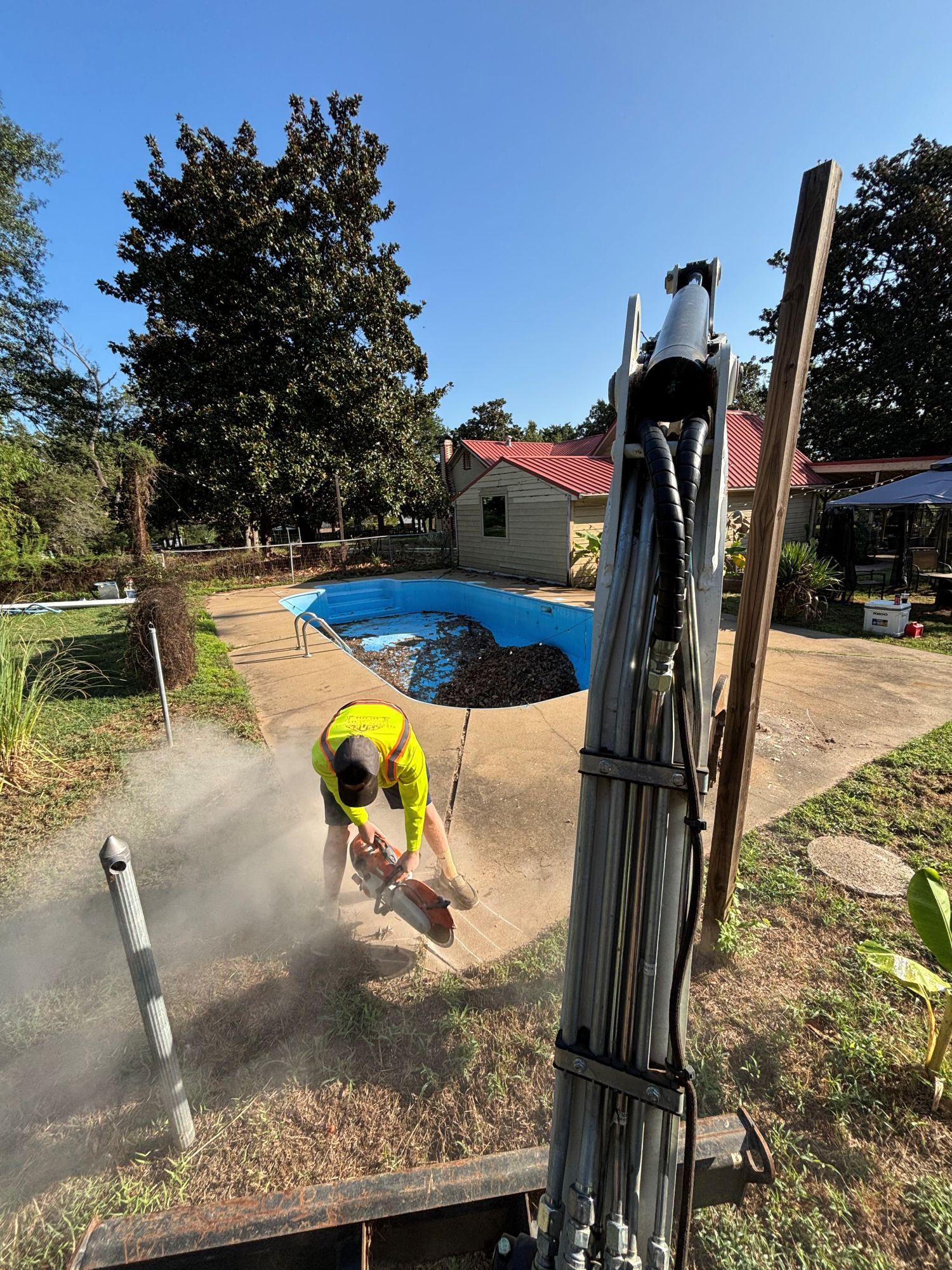 Person cutting concrete near a pool, with a lift in the foreground.