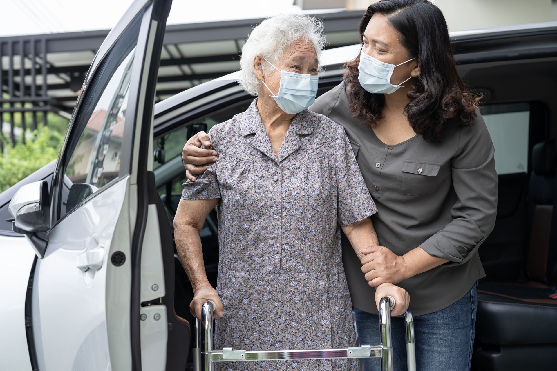 A woman is helping an elderly woman with a walker get out of a car.