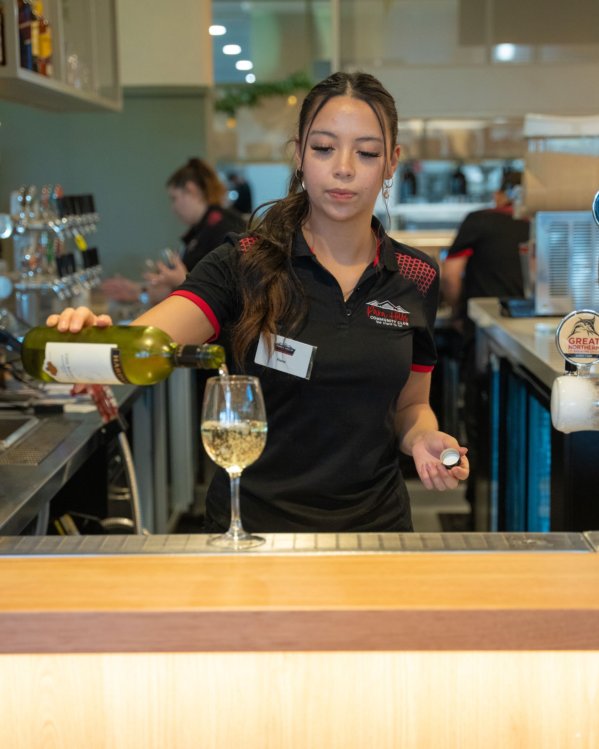 A woman is pouring wine into a glass at a bar at Para Hills Community Club