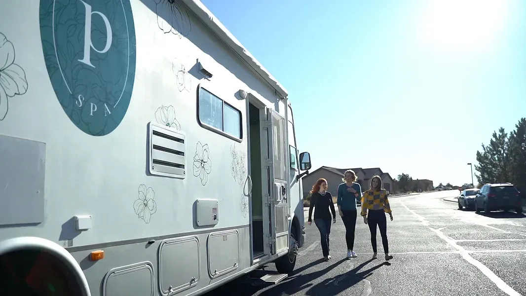 three women walking in front of the Spa on wheels bus, beauty bus & rejuvenation vehicle