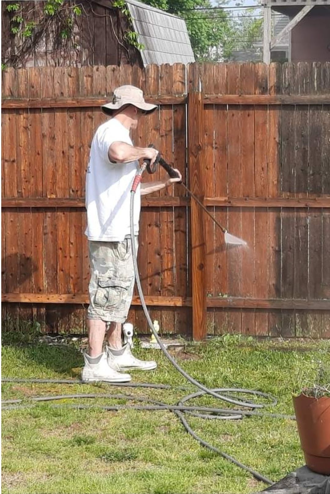 A man is cleaning a wooden fence with a pressure washer.