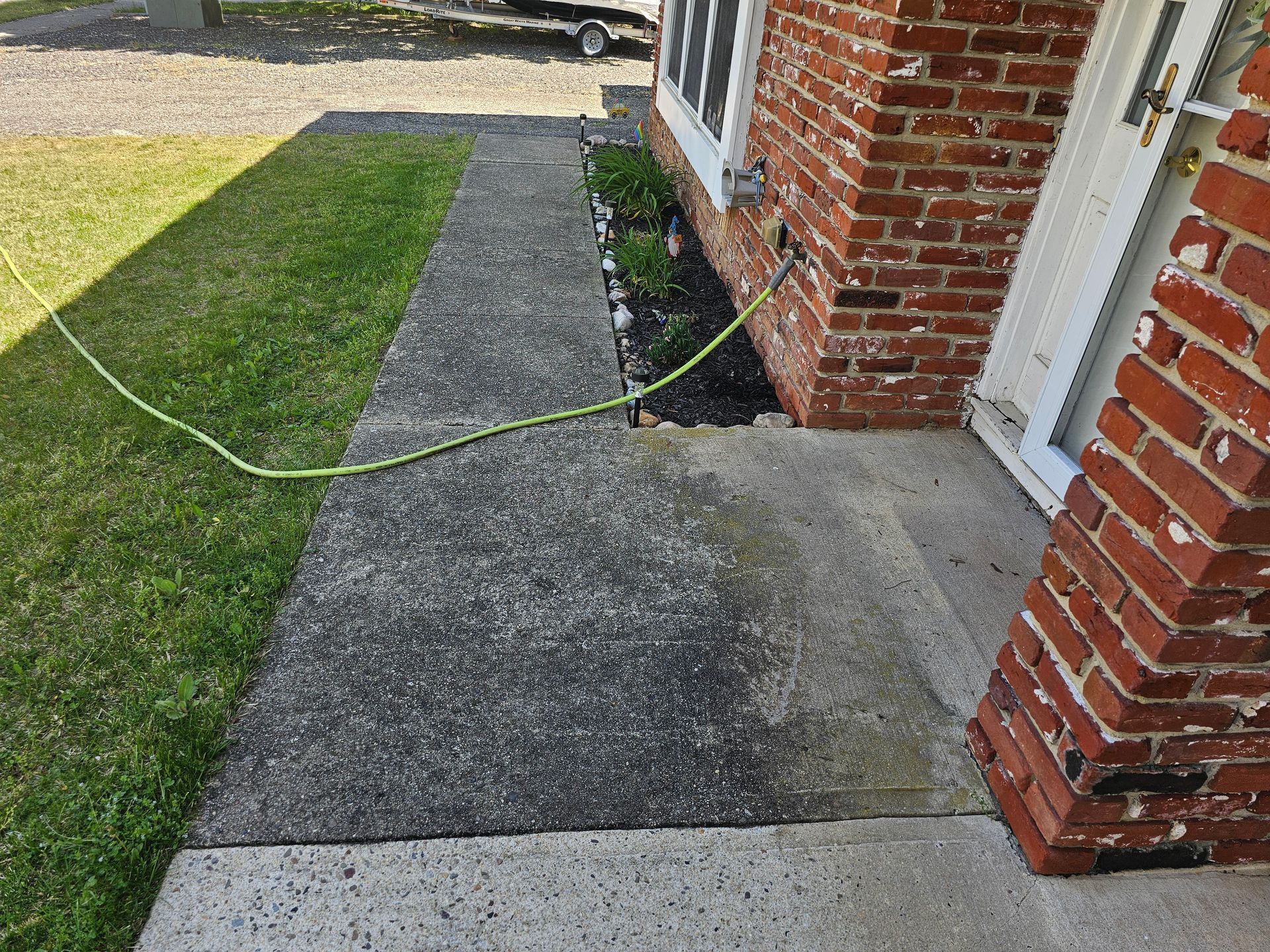 A hose is attached to the sidewalk in front of a brick house.