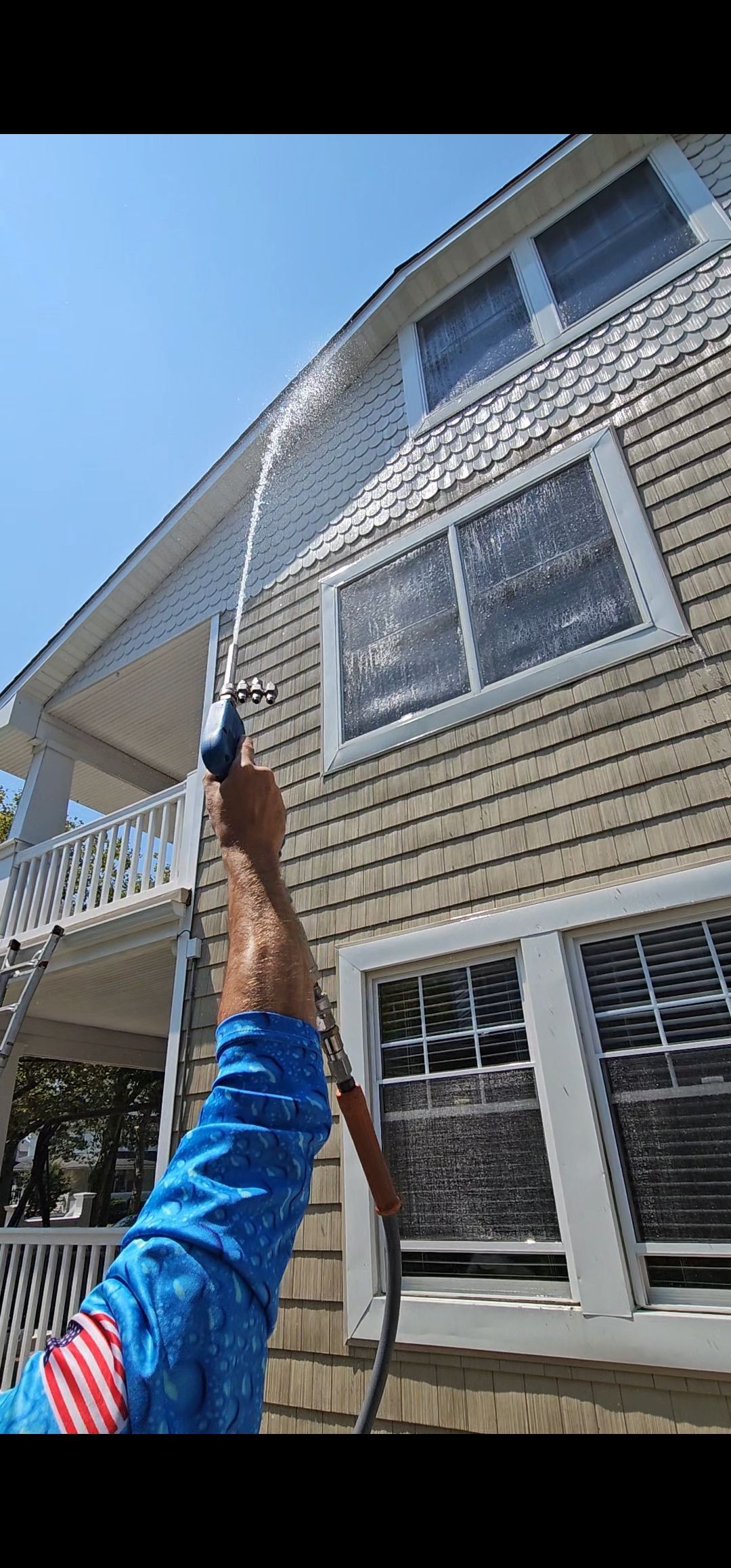 A man is washing the side of a house with a hose.