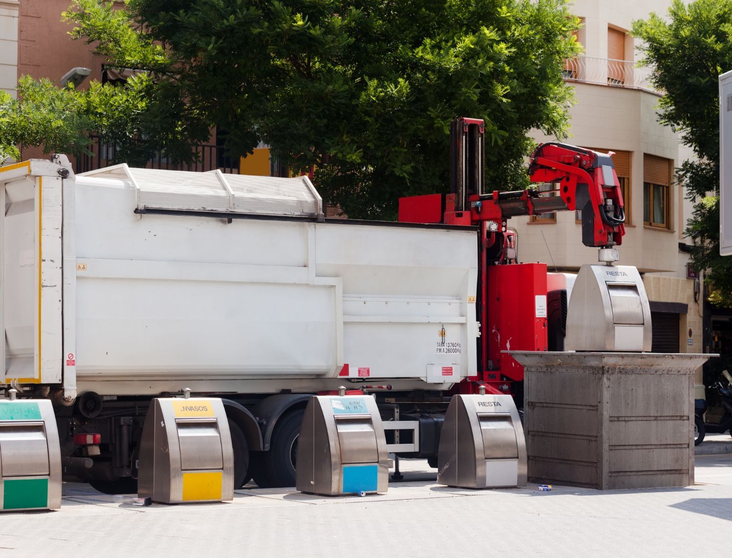 A red and white garbage truck is parked next to a row of trash cans.