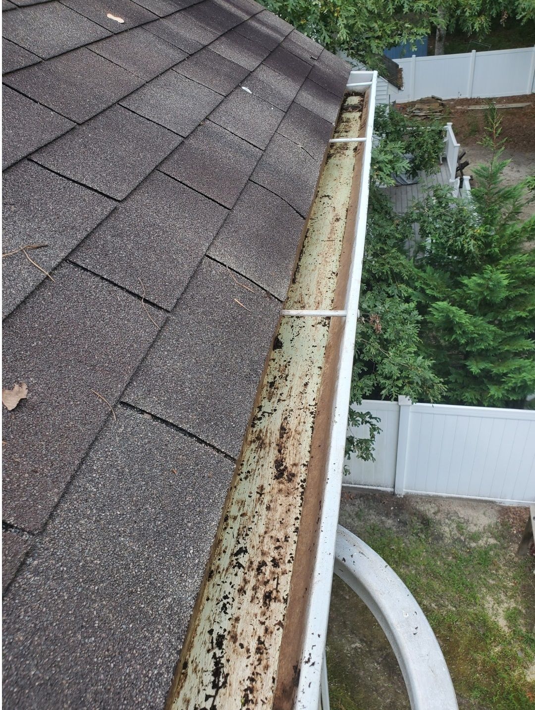 A gutter is sitting on top of a roof next to a white fence.