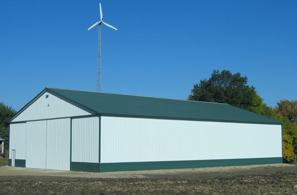 A white building with a green roof and a wind turbine in the background.