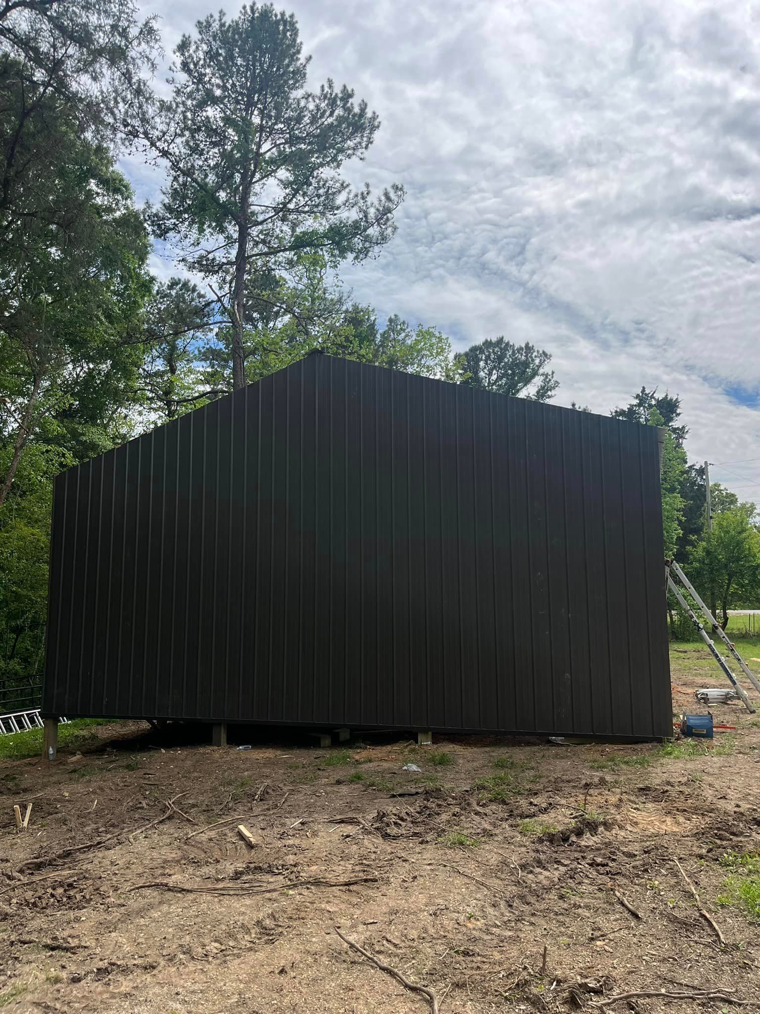 A black metal shed is sitting in the middle of a dirt field.