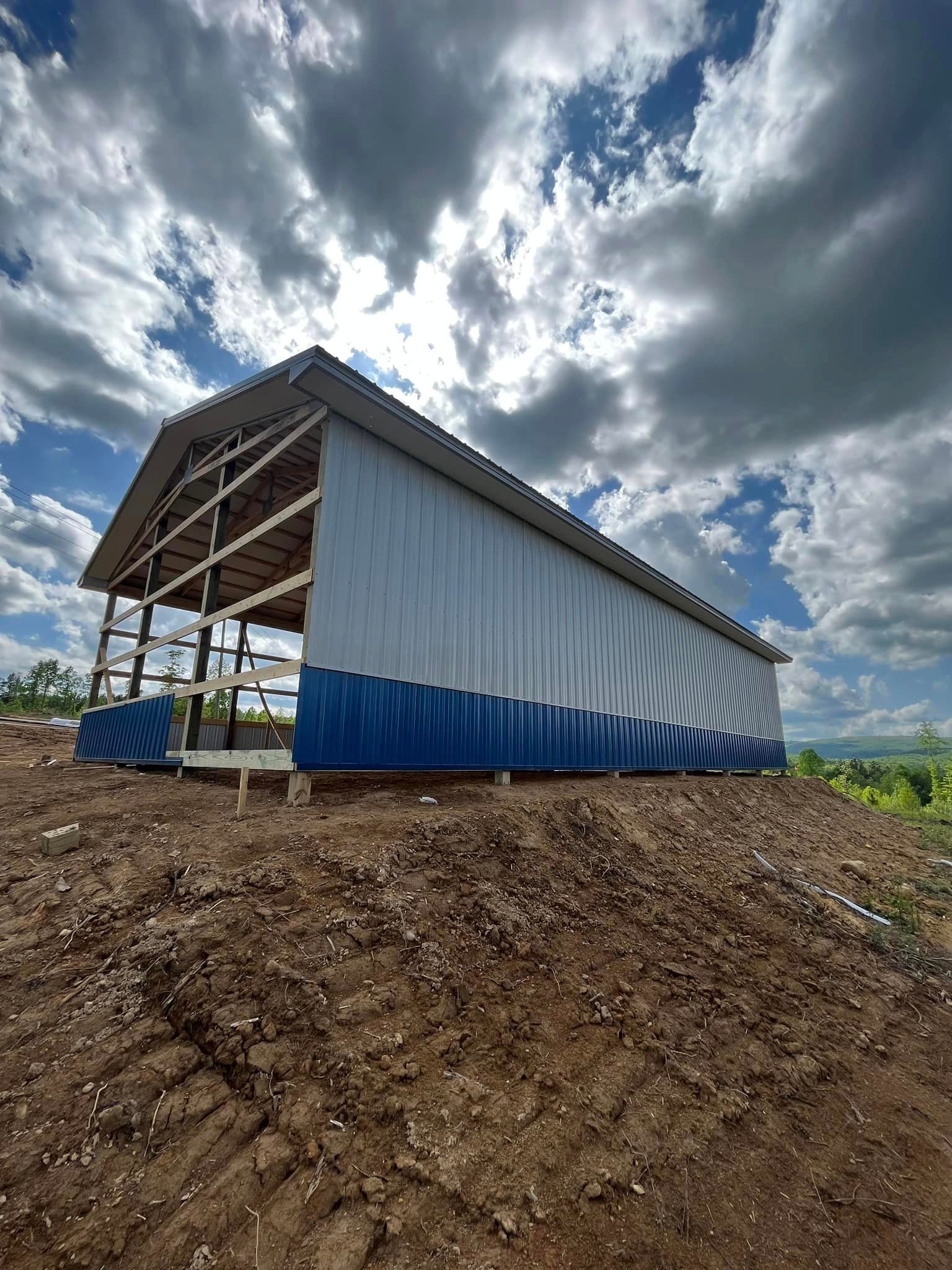 A blue and white barn is sitting on top of a dirt hill.