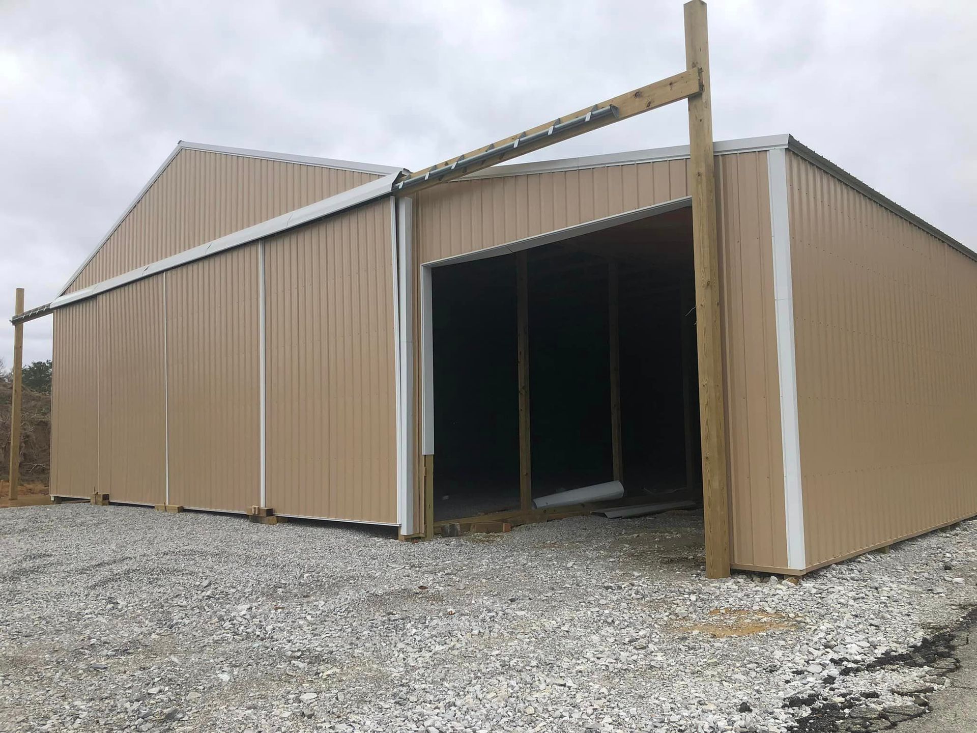 A large metal building with a large door is sitting on top of a gravel lot.
