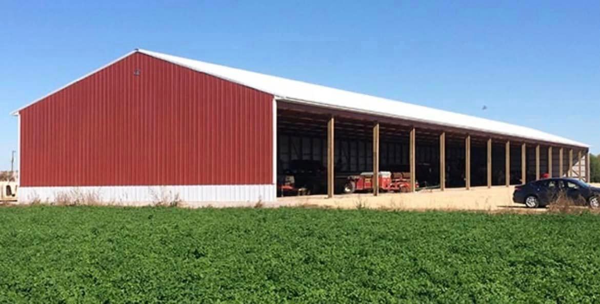 A red barn with a white roof is sitting in the middle of a green field.
