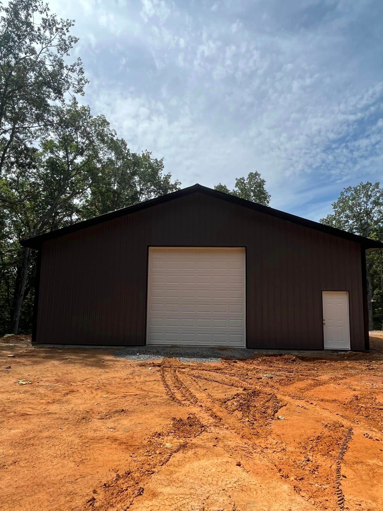 A large brown building with a white garage door is sitting in the middle of a dirt field.